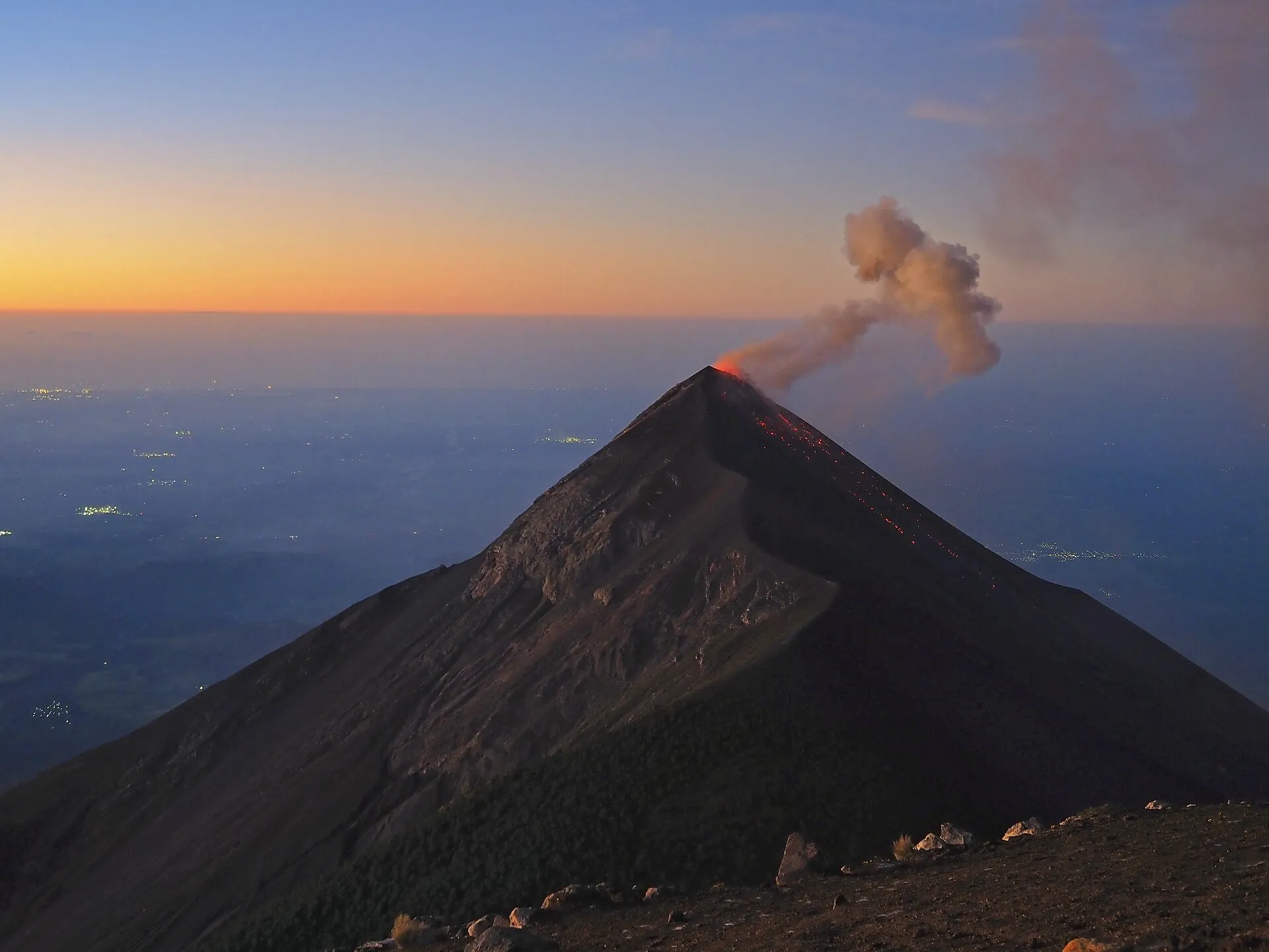 Dawn on the summit of Acatenango: looking down on the cone of Volcán de Fuego with an ash plume, an orange band on the horizon