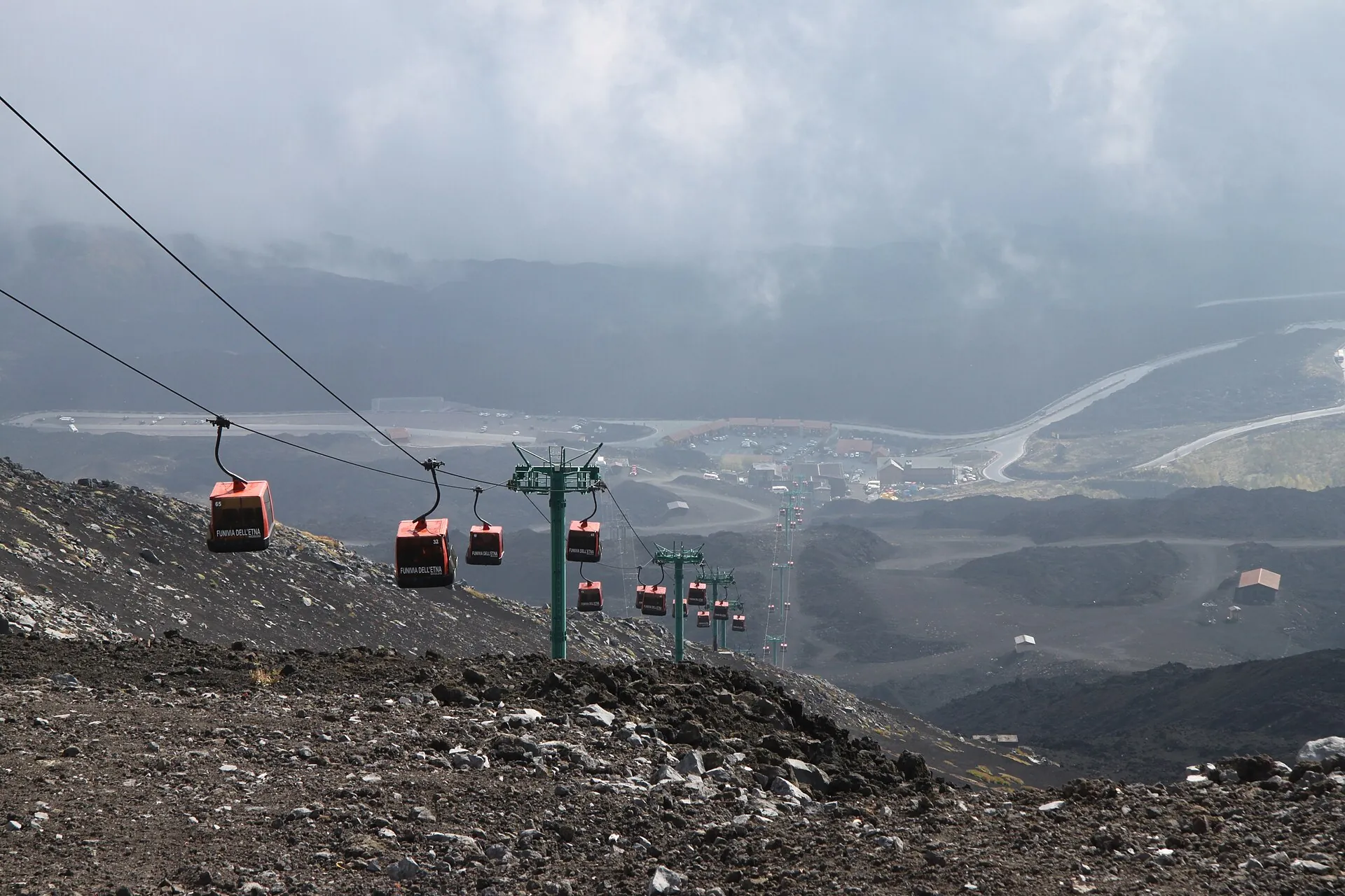 Gondolas of the Funivia dell'Etna above black lava, Rifugio Sapienza and the hairpins of the road below