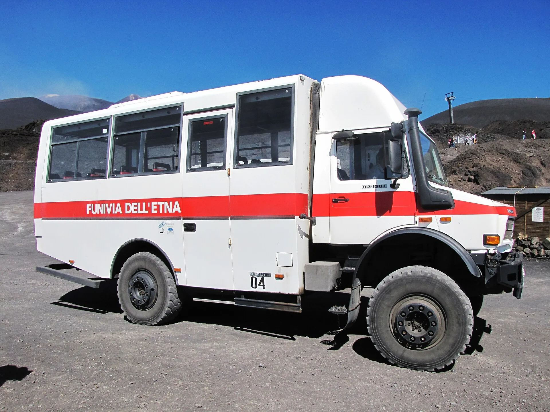 A white Unimog 4x4 bus of the Funivia dell'Etna with a red stripe standing on black lava ground