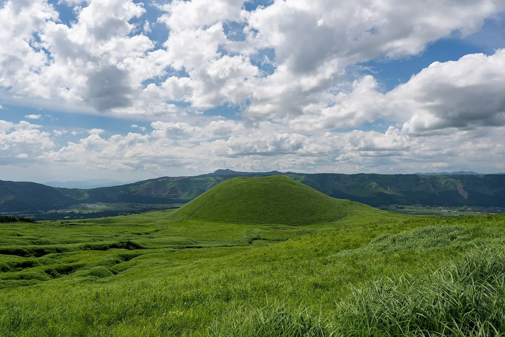 Der grasbewachsene Schlackenkegel Komezuka in der Caldera des Aso unter Wolkenhimmel