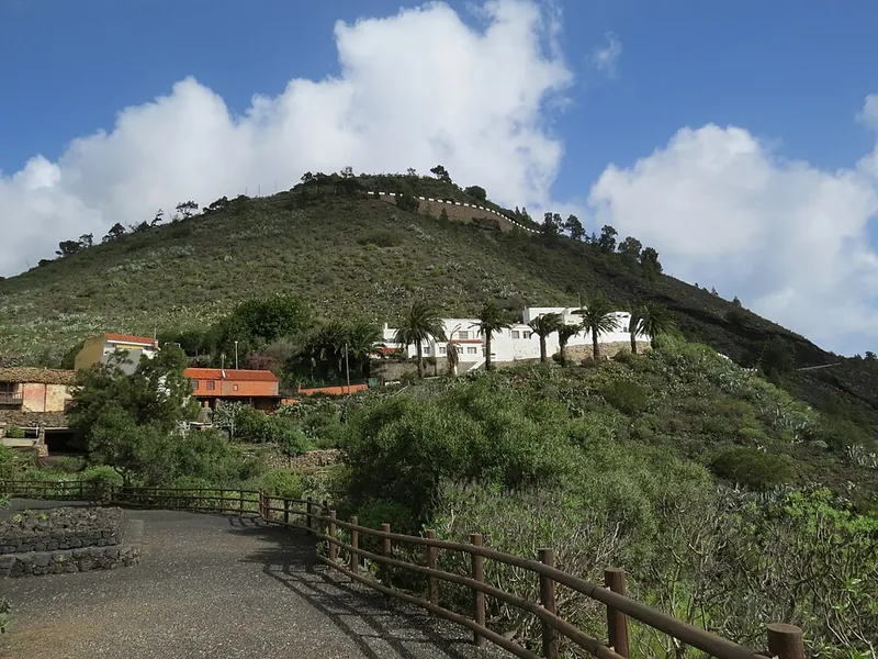 Das Caserío de Bandama mit weißen Häusern und Palmen, dahinter der Pico de Bandama unter Wolken