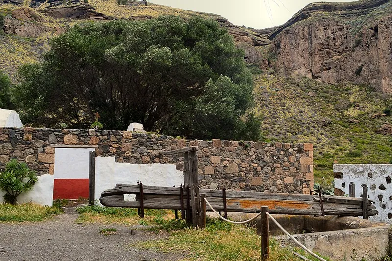Alte steinerne Weinpresse mit Holzbalken vor einer weiß-roten Hofmauer am Kraterboden der Caldera de Bandama