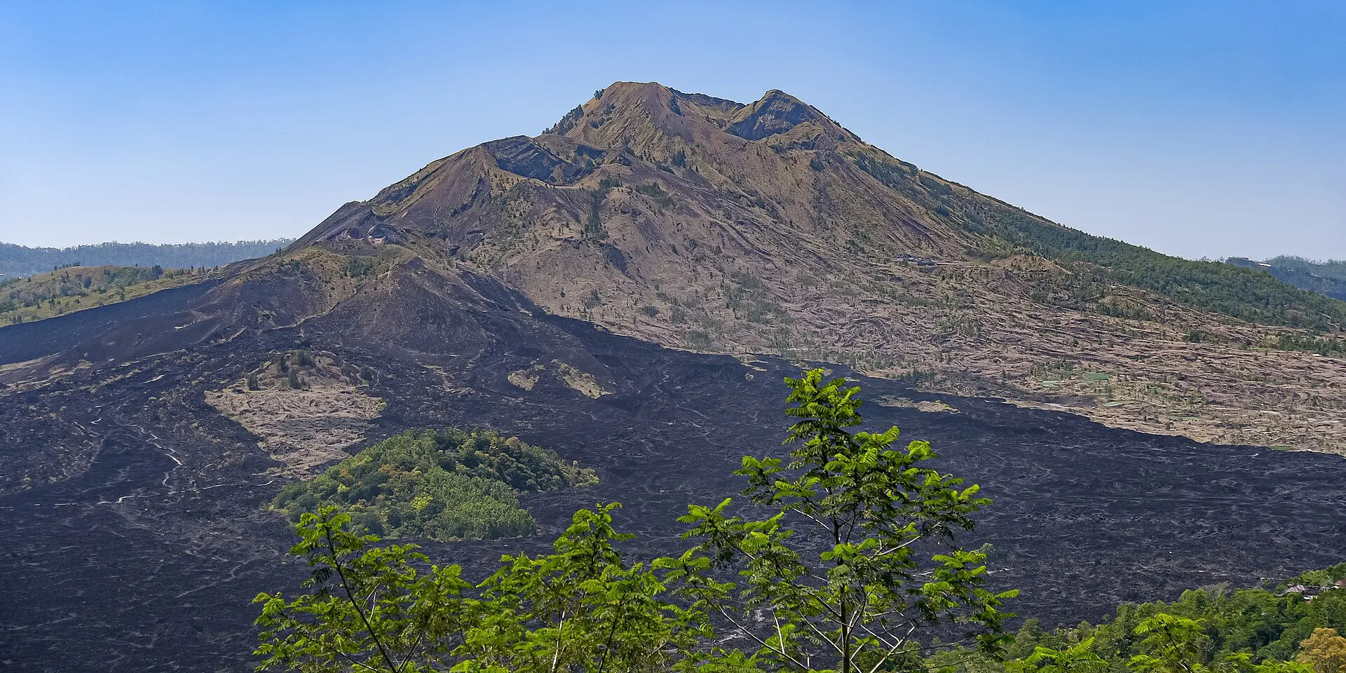 The cone of Mount Batur by day, with the black lava fields of the Kintamani caldera in front of it