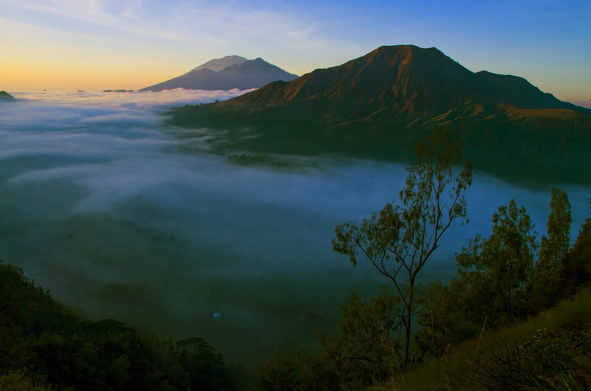 Morning mist in the Batur caldera on Bali: banks of fog over the caldera floor, with the cones of Abang and Agung behind in first light