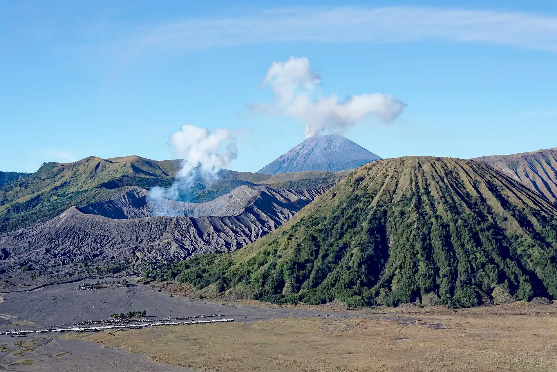 View from the caldera rim in the morning: Bromo's smoking crater, the green, ribbed cone of Batok on the right, Semeru with an ash cloud behind it