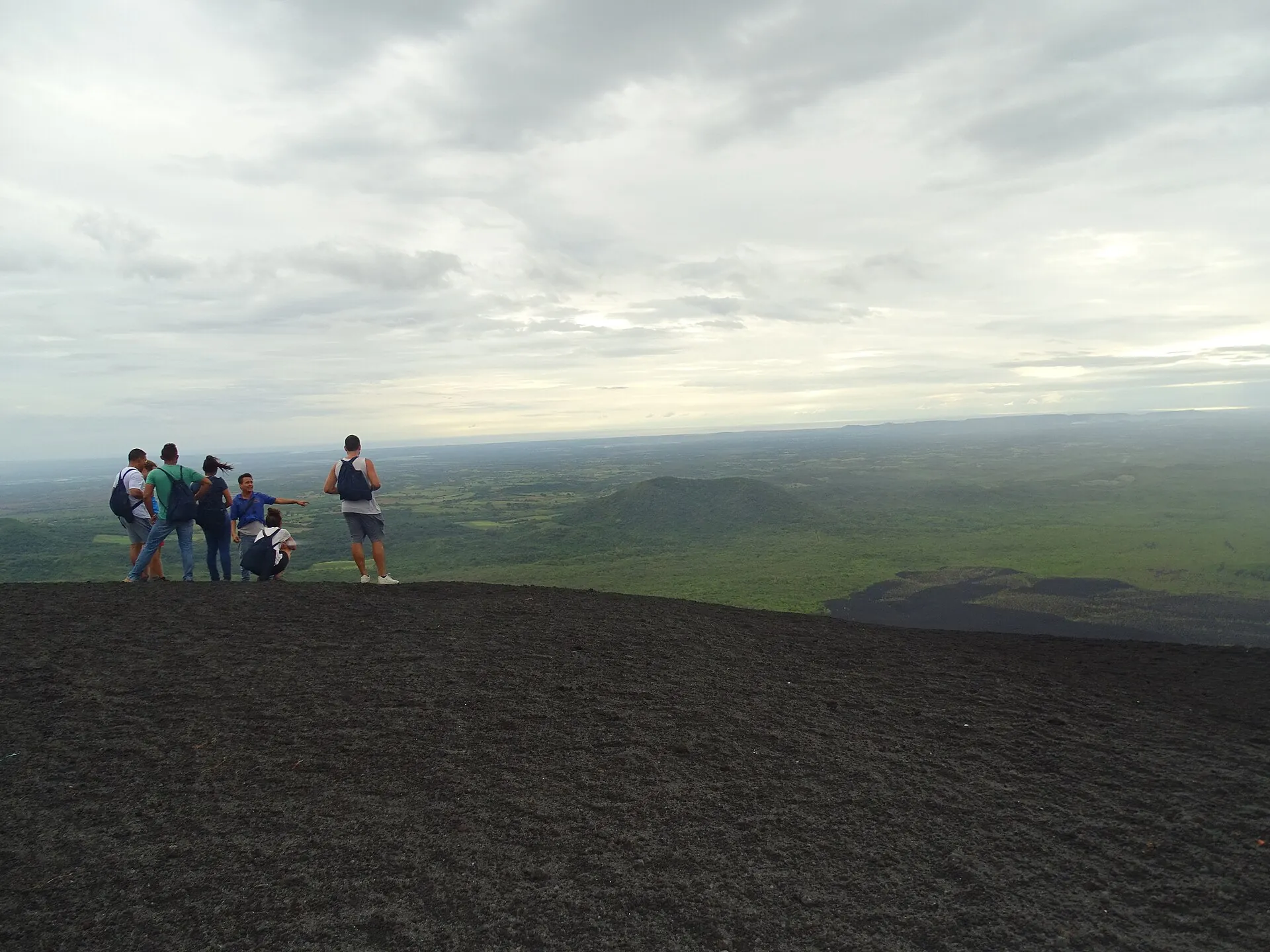 Eine kleine Gruppe steht auf dem Grat des Cerro Negro, dahinter die grüne Ebene um León