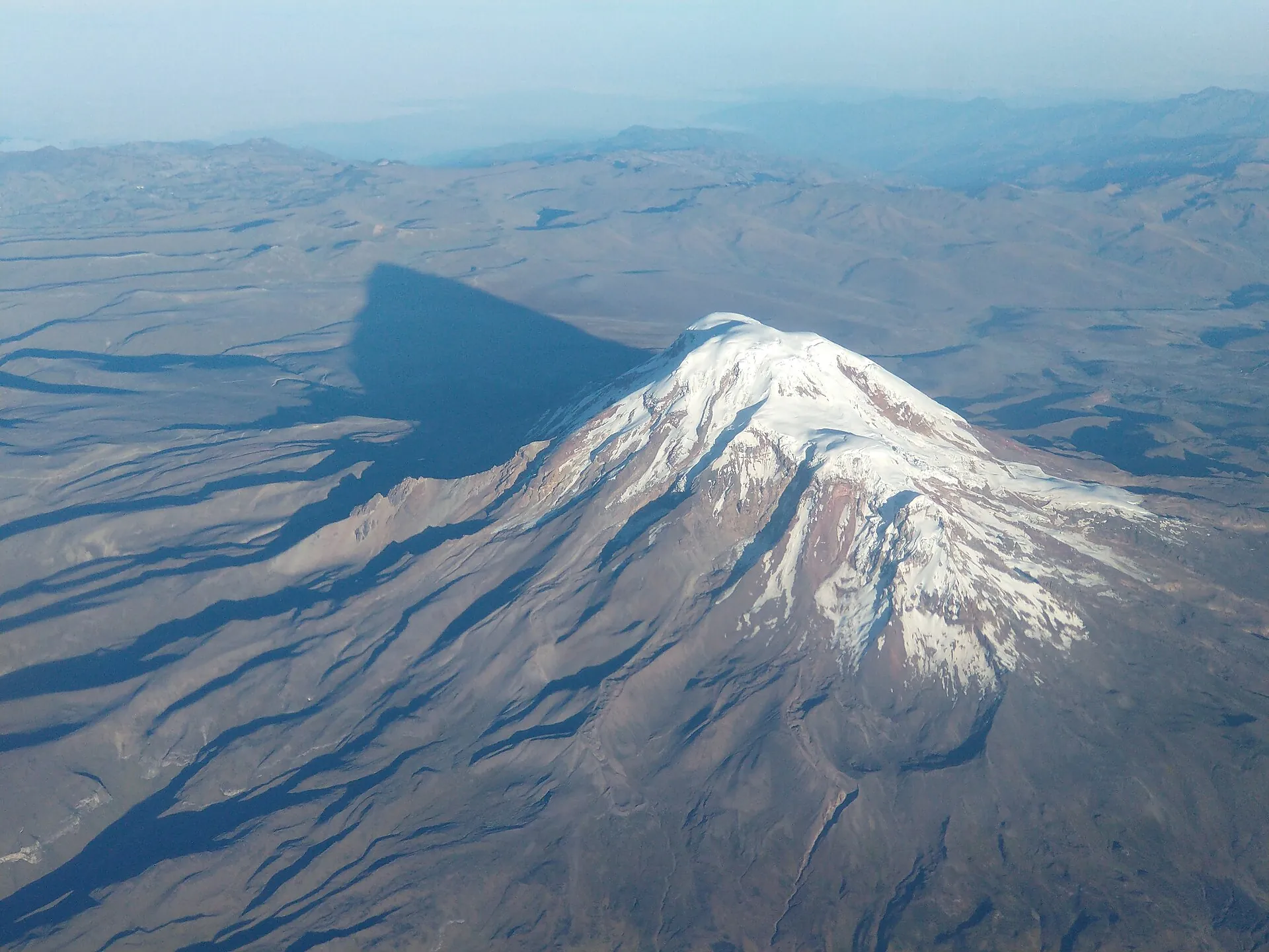 Der Chimborazo aus der Luft: die vergletscherte Gipfelkuppe wirft einen langen Schatten über die braune Hochebene