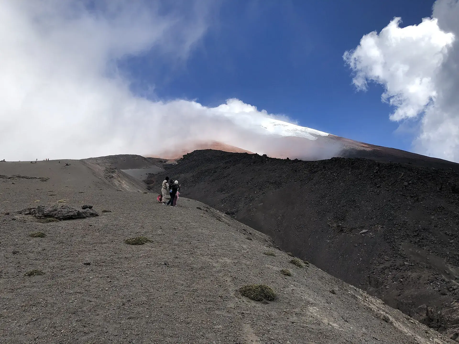 Wanderer auf dem grauen Aschehang oberhalb des Parkplatzes am Cotopaxi, der Gipfel in Wolken