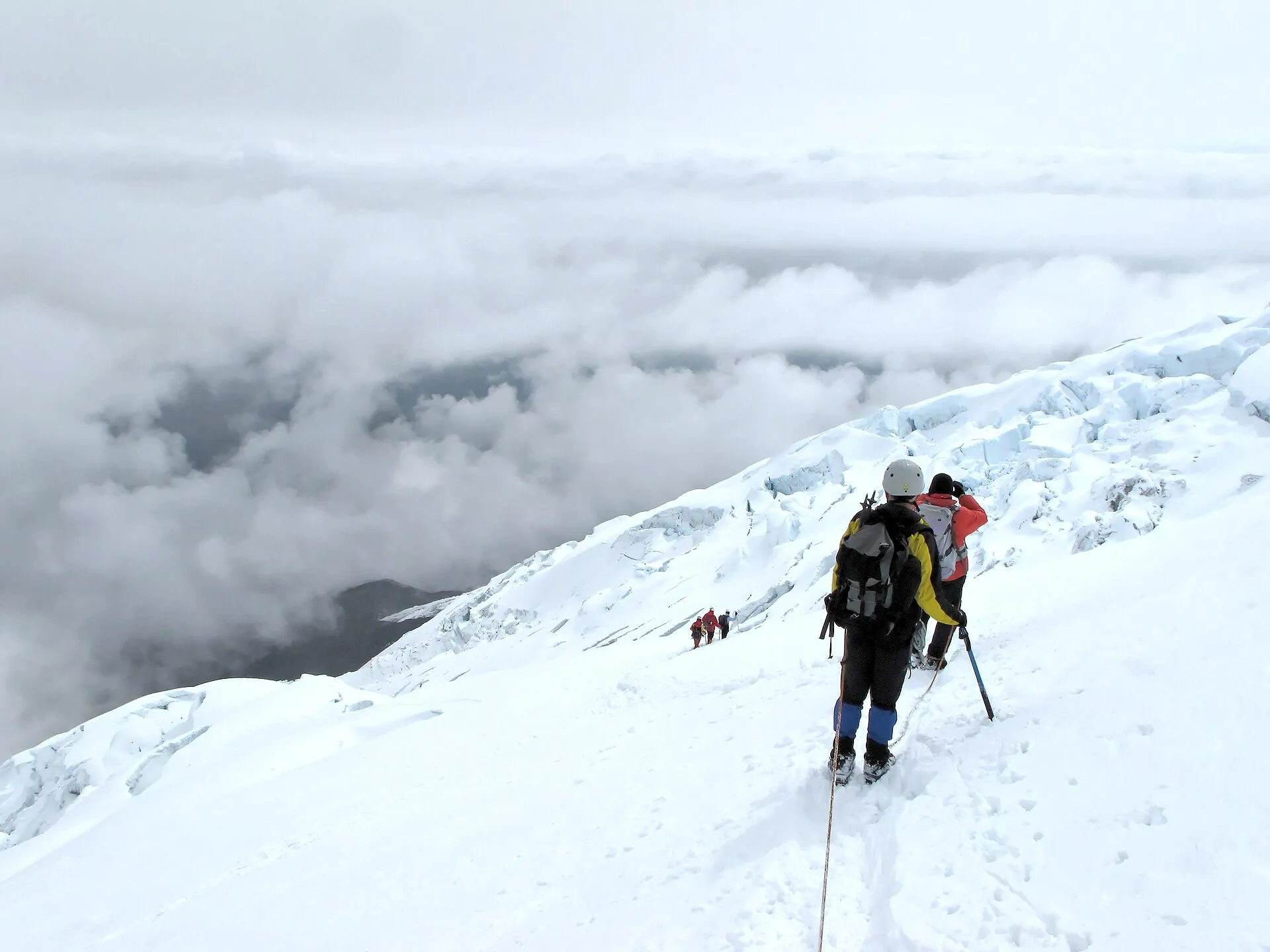 Zwei Bergsteiger am Seil auf dem Gletscher der Normalroute des Cotopaxi, darunter ein Wolkenmeer