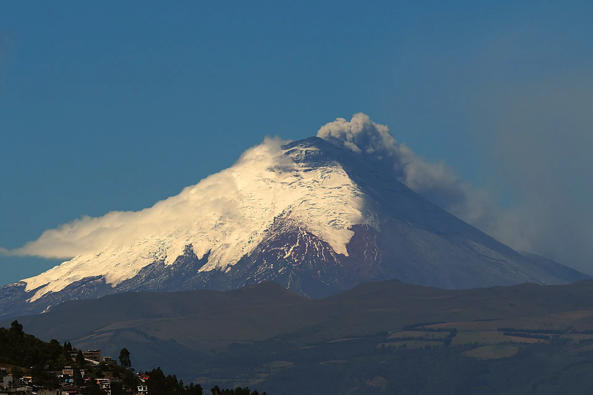 Der Cotopaxi stößt im August 2015 eine graue Aschesäule aus, im Vordergrund die Häuser von Quito