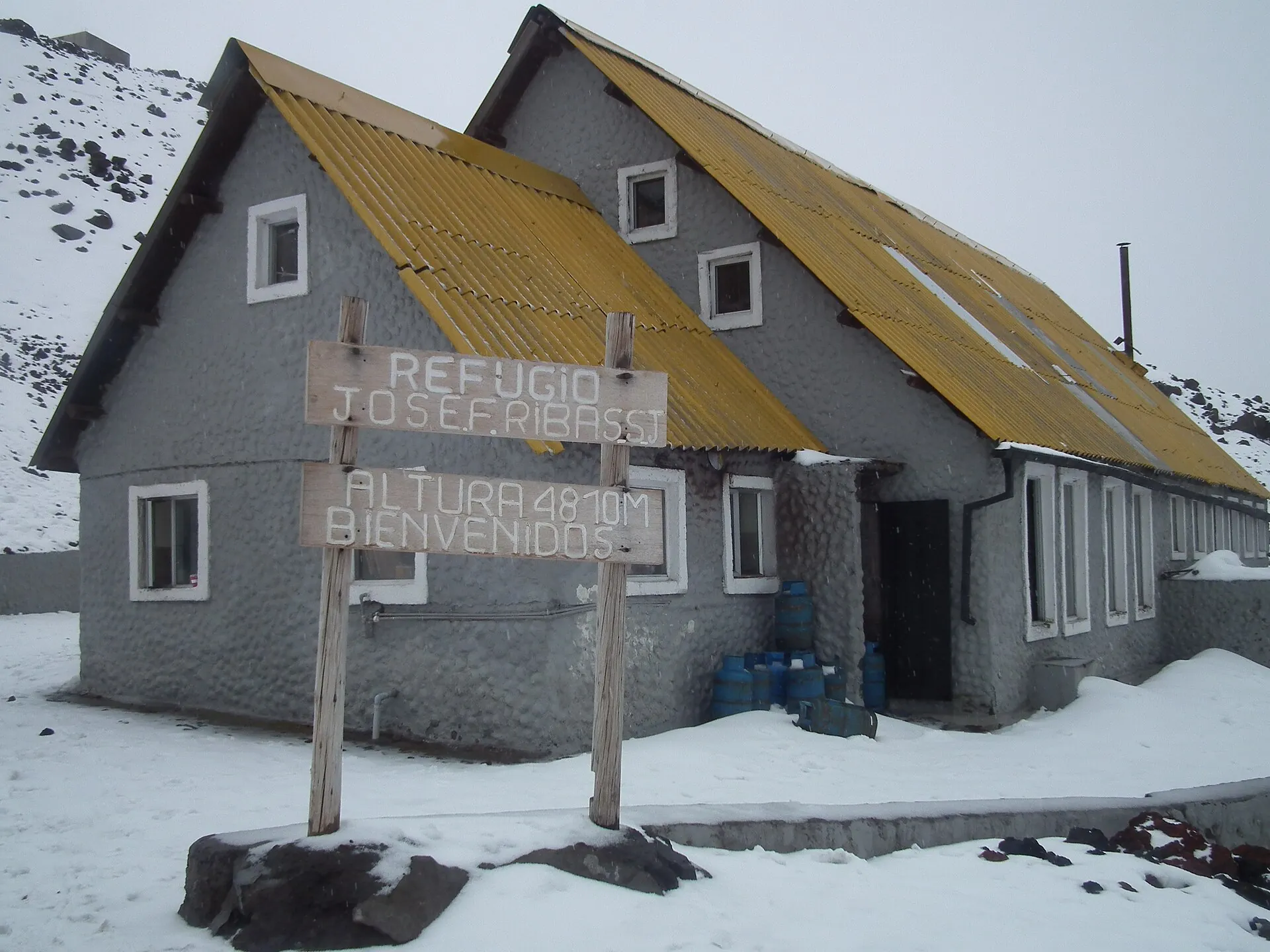 Das Refugio José Rivas am Cotopaxi mit gelbem Dach, Neuschnee auf dem Aschehang, ein Wanderer davor