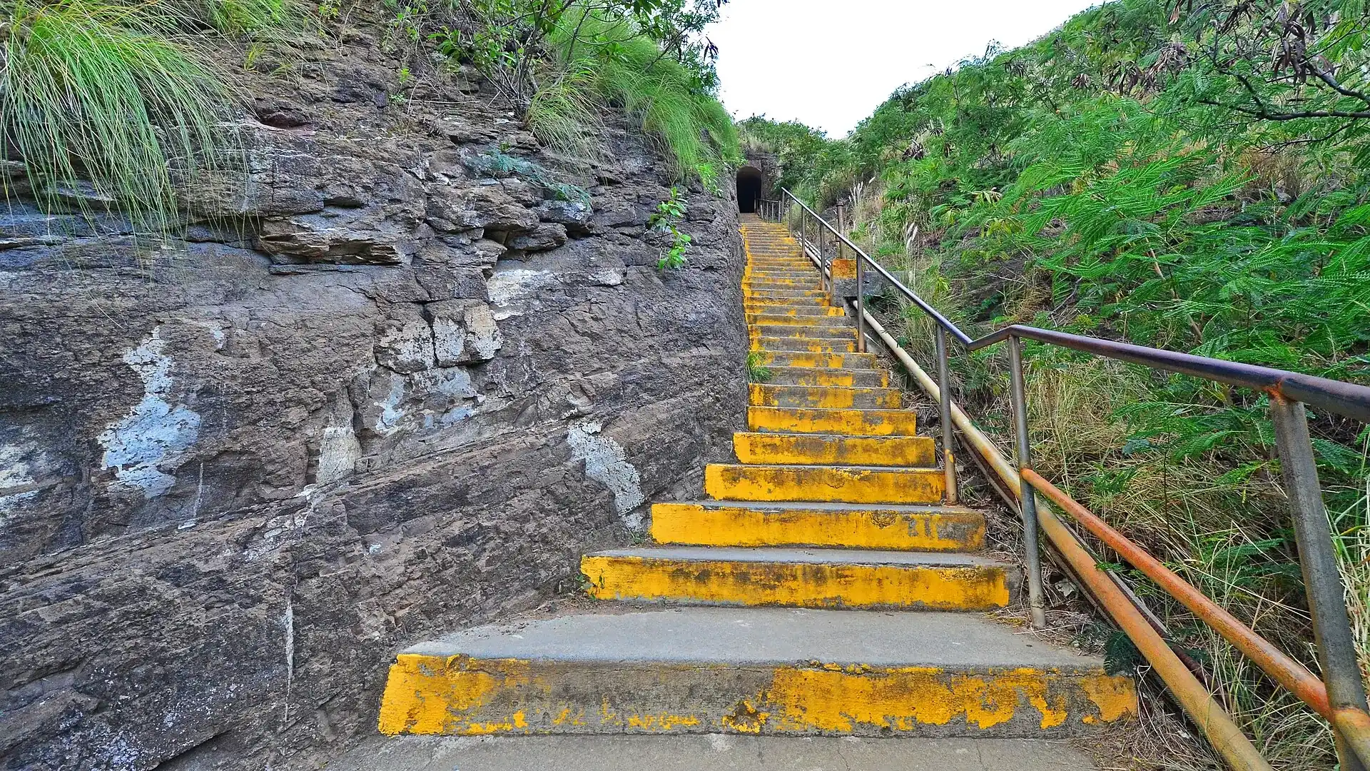 Yellow-edged concrete steps on the Diamond Head Summit Trail climb steeply between tuff walls to a tunnel entrance