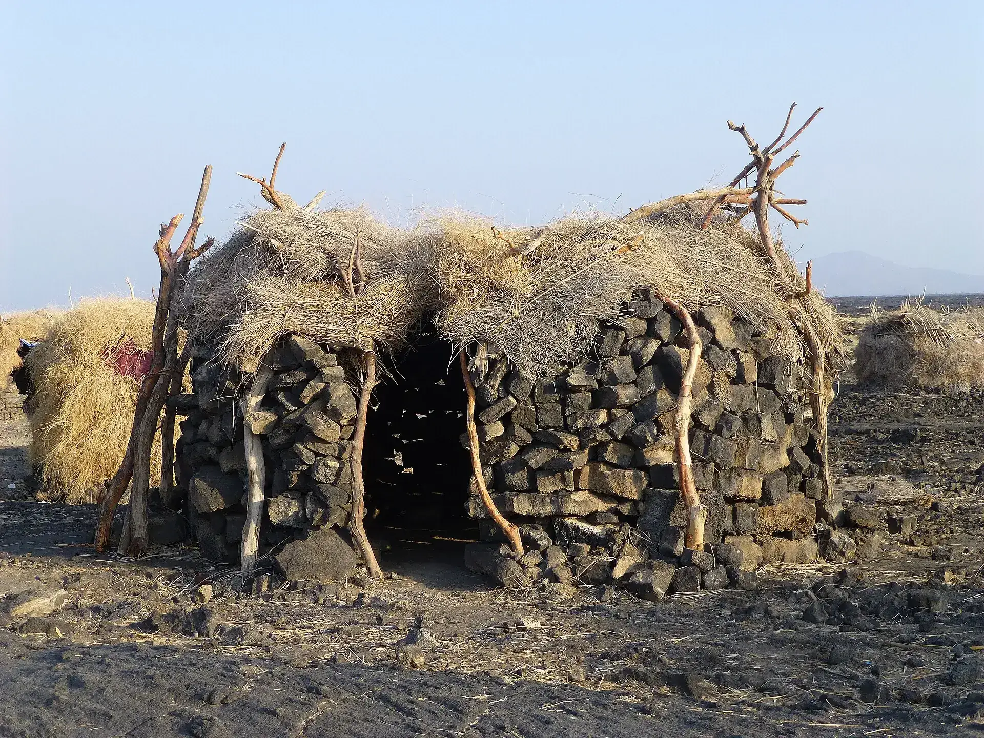 A stone hut with a thatched roof at the Dodom base camp below Erta Ale, the flat Danakil plain behind it