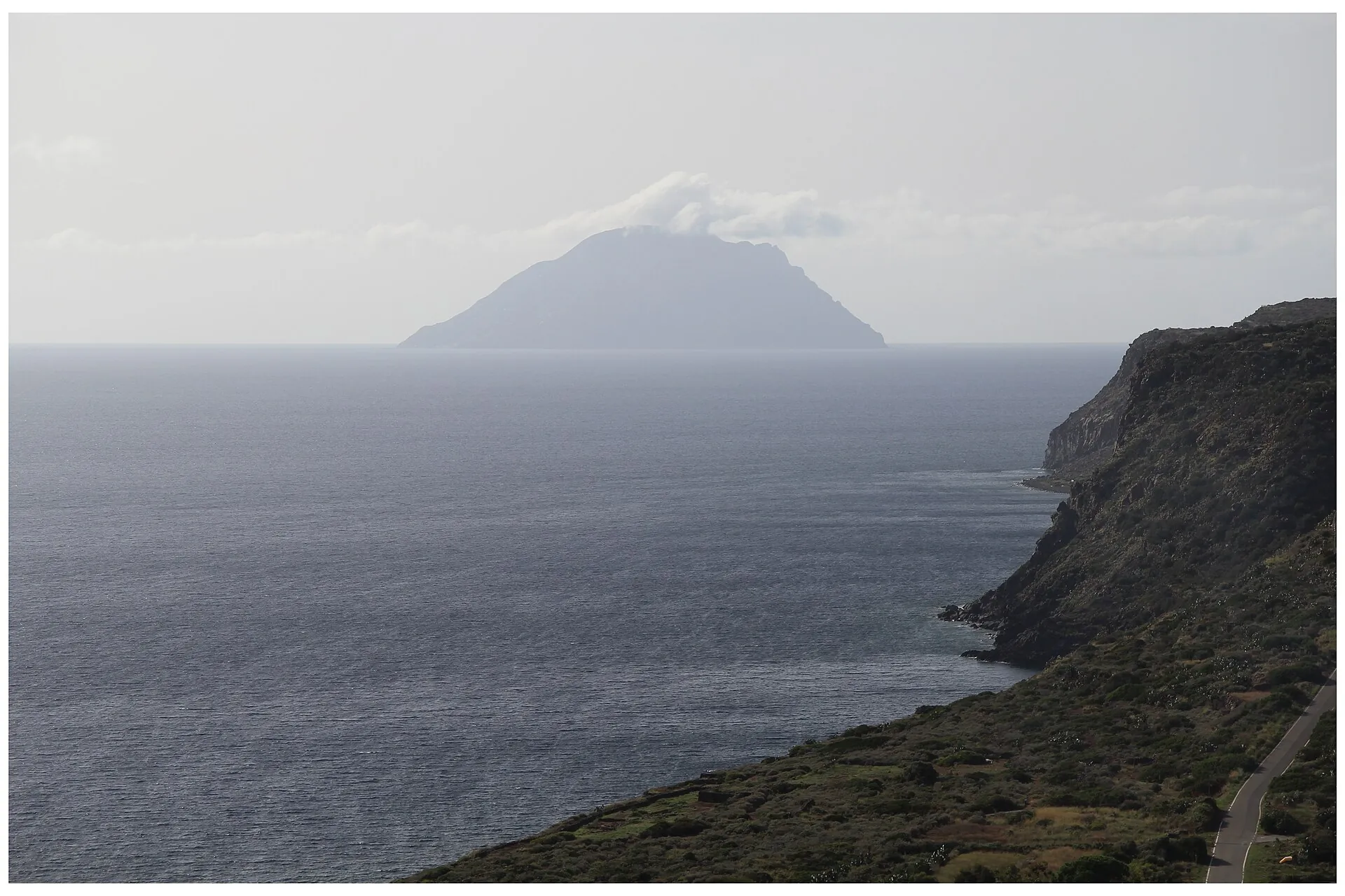 View from Filicudi across to Alicudi: a single dark cone in the haze above the sea