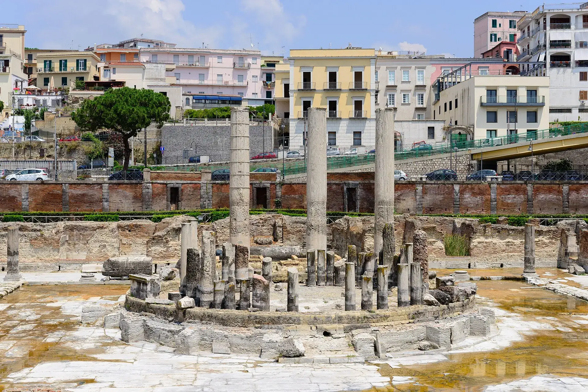 Die Säulen des Macellum in Pozzuoli mit Bohrmuschelspuren, dahinter die Häuser der Stadt