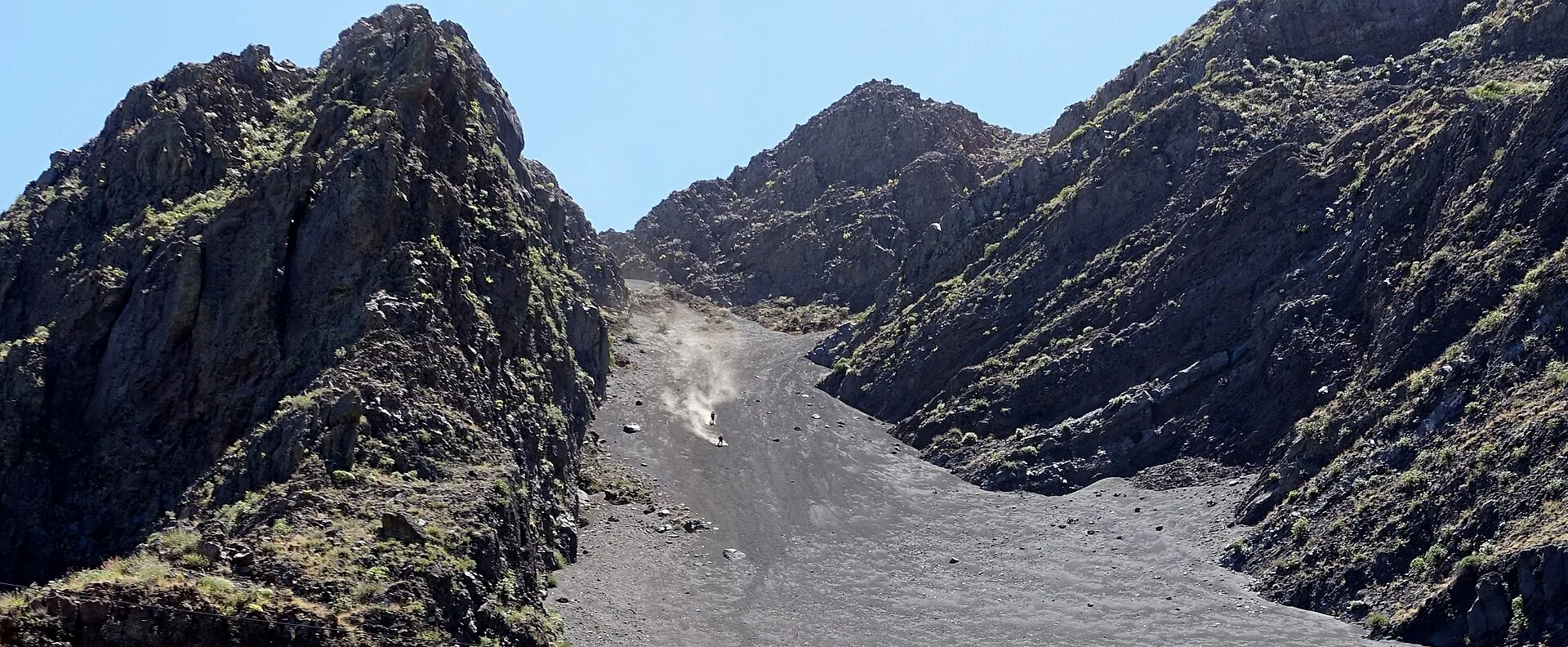 Abstieg vom Pico do Fogo: eine Staubfahne über der grauen Ascherinne zwischen dunklen Lavafelsen