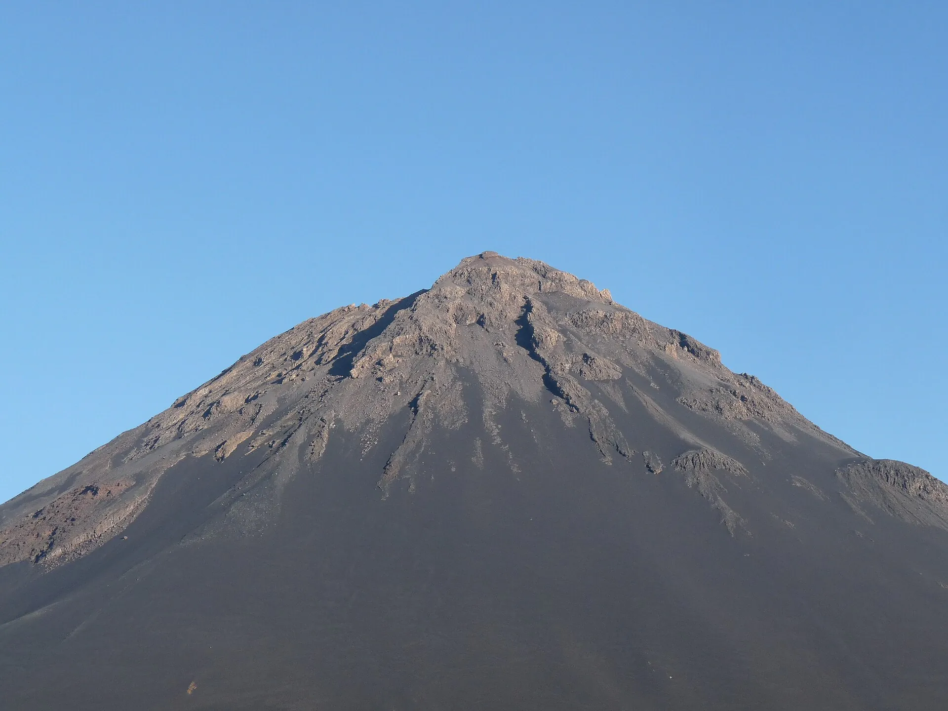 Der Pico do Fogo bei klarem Himmel: ein fast symmetrischer Kegel aus dunkler Asche mit gezacktem Kraterrand