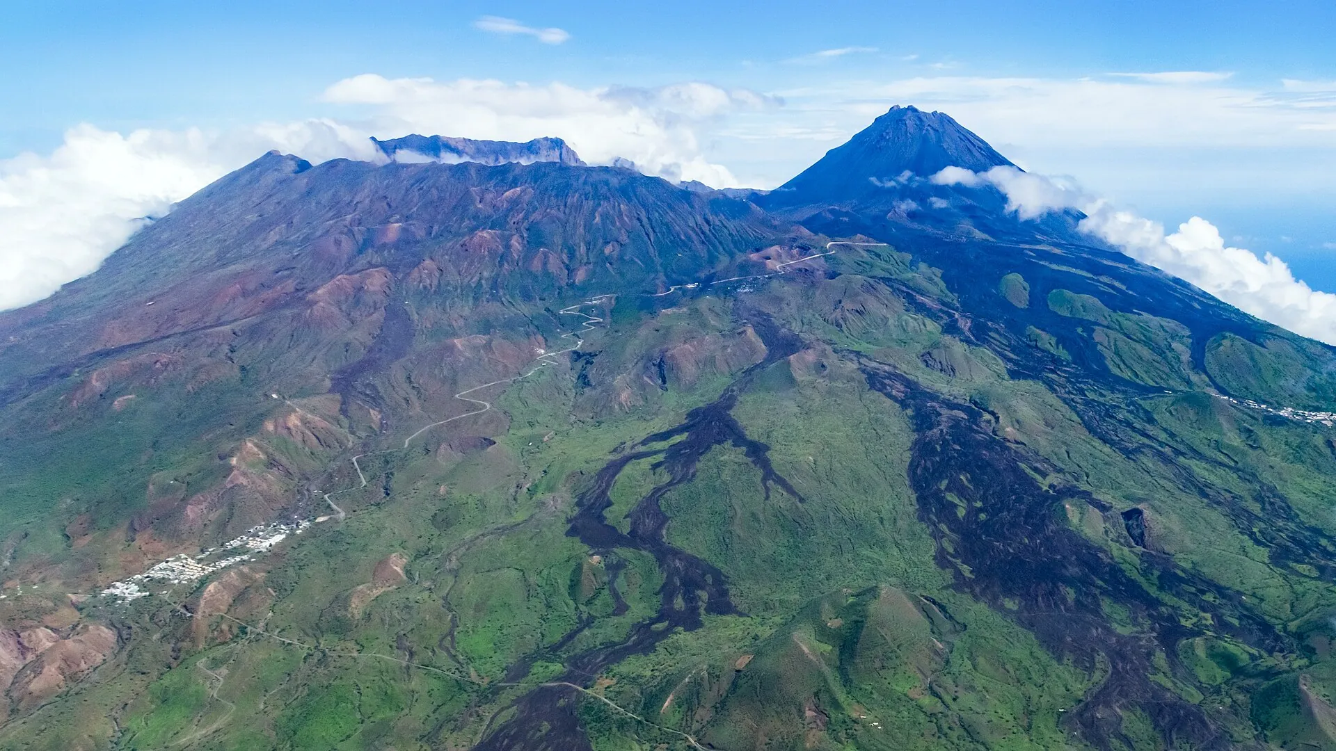 Luftaufnahme der Insel Fogo von Süden: die grüne Bordeira-Wand, die schwarzen Lavaströme in der Caldera und der Kegel des Pico do Fogo