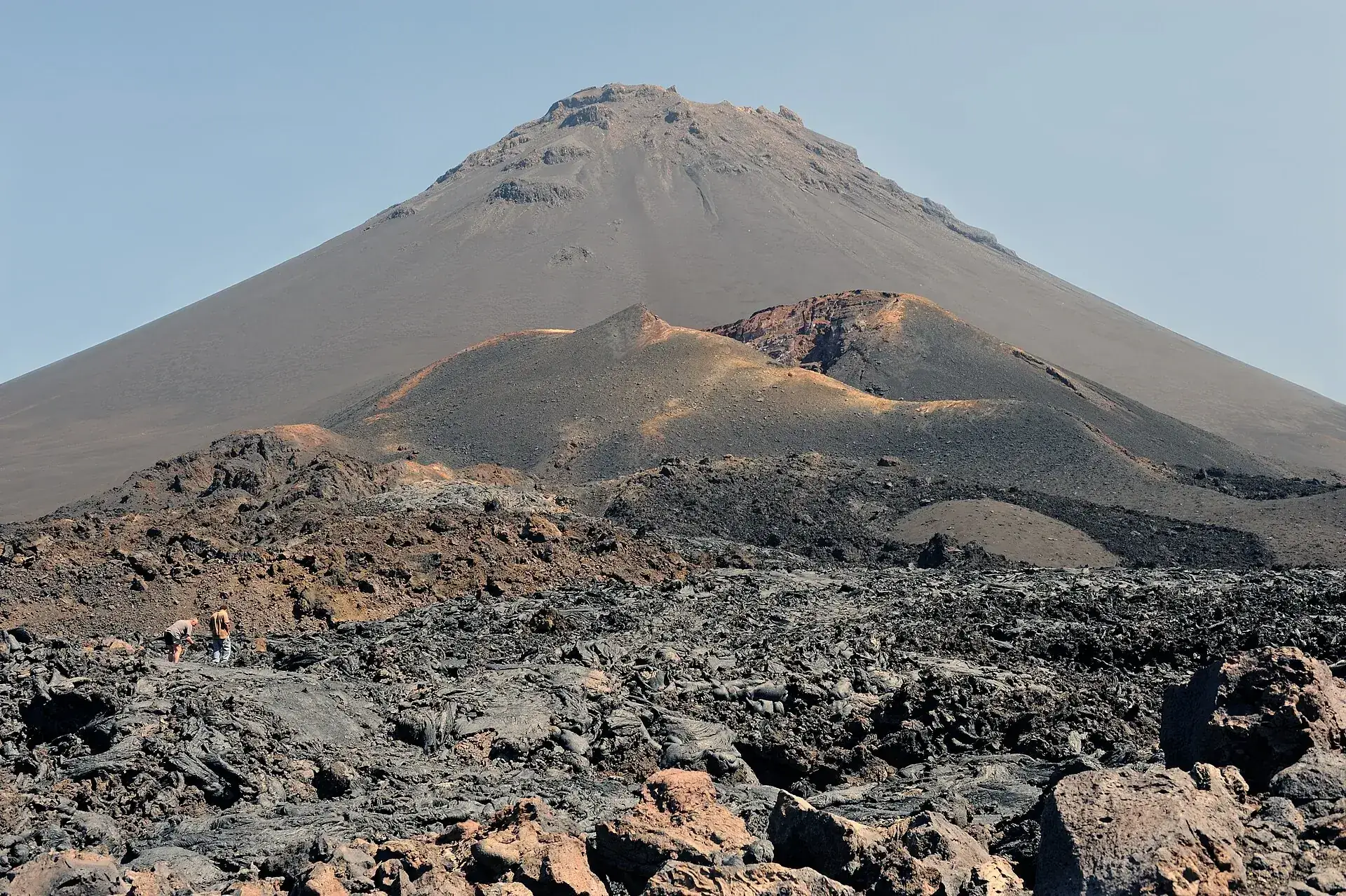 Der Pico do Fogo von der Caldera aus: der graue Aschekegel, davor der rot und ocker gefärbte Krater des Pico Pequeno, im Vordergrund schwarze Blocklava
