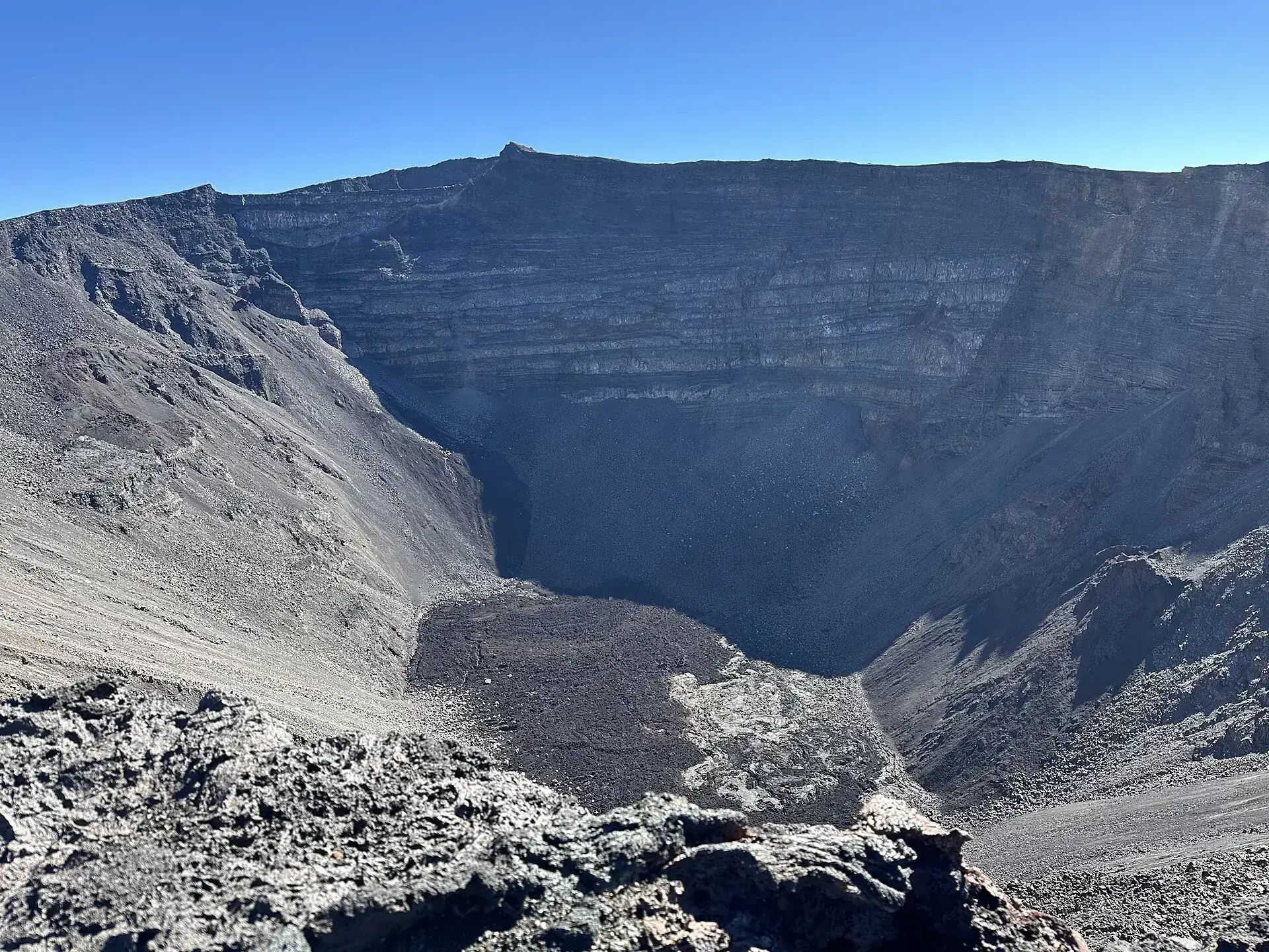 Looking into the Dolomieu crater of Piton de la Fournaise: vertical, layered walls, the gray crater floor far below