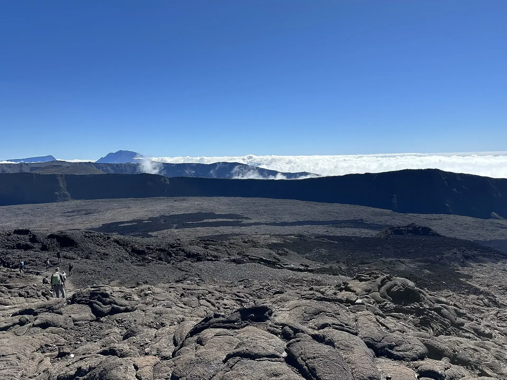 Hikers on the rough gratons lava in the Enclos Fouqué, behind them the Rempart and a sea of clouds over Réunion