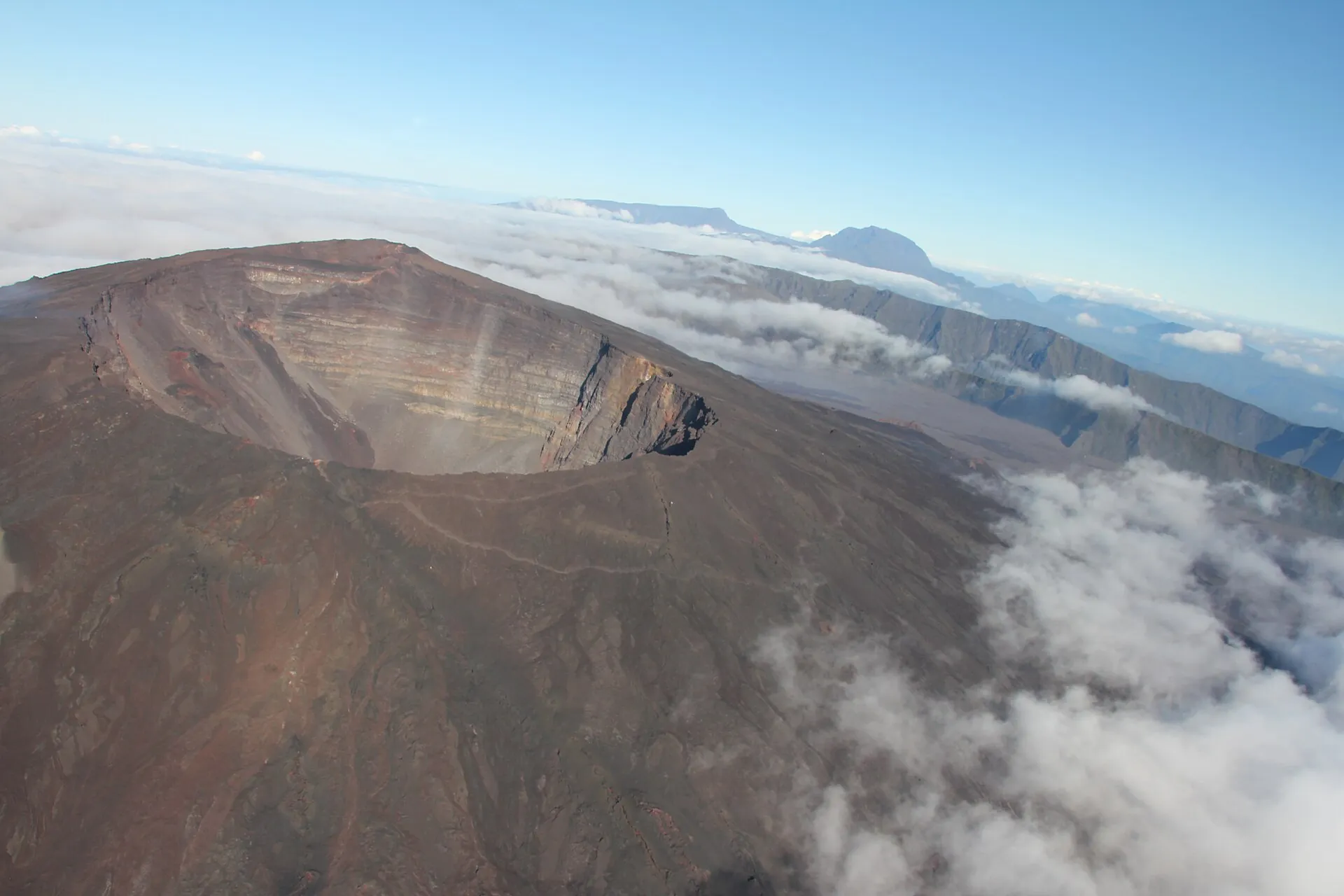 Aerial view of the summit of Piton de la Fournaise: the cone with the collapsed Dolomieu crater above a sea of clouds, Piton des Neiges behind