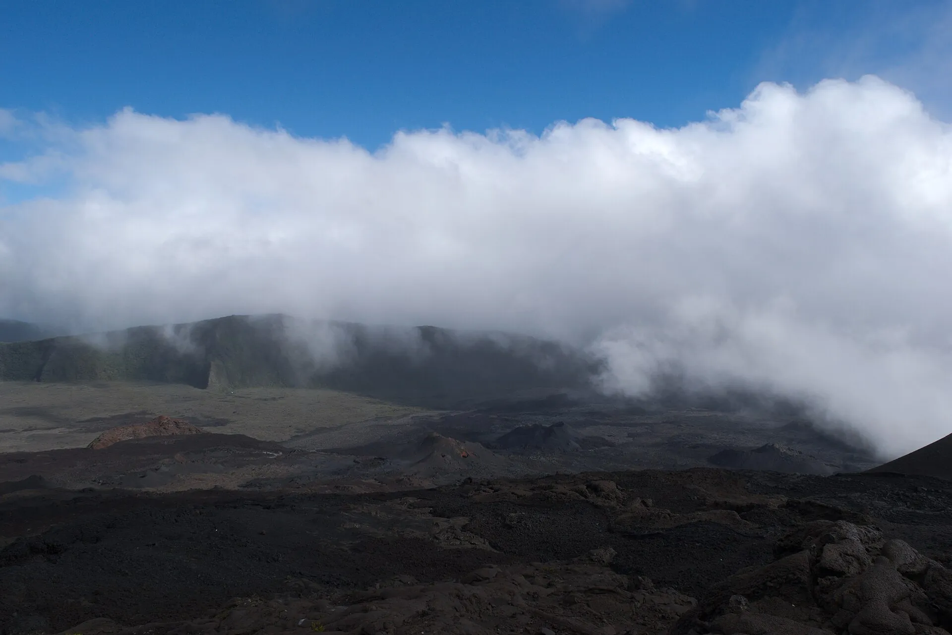 A dense bank of cloud pushing over the edge of the Rempart into the Enclos Fouqué, the dark lava field below