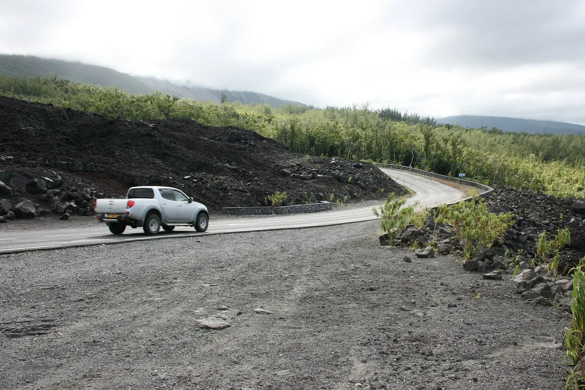 The Route des Laves (RN2) in the Grand Brûlé: a pickup on the road between black lava and young green on the slope