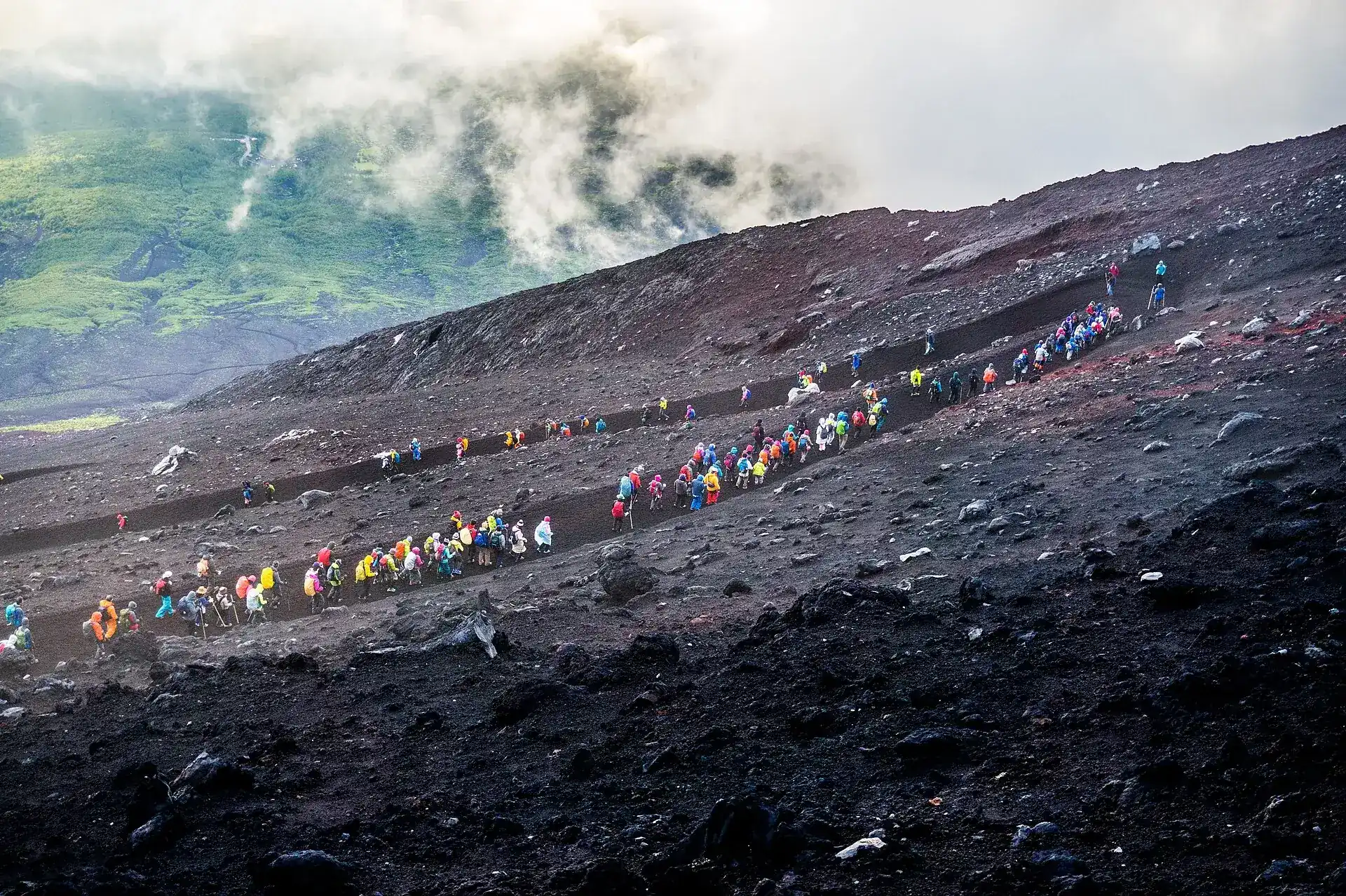 A long line of climbers in bright jackets descending the switchbacks of the Yoshida Trail on Mount Fuji shortly after sunrise