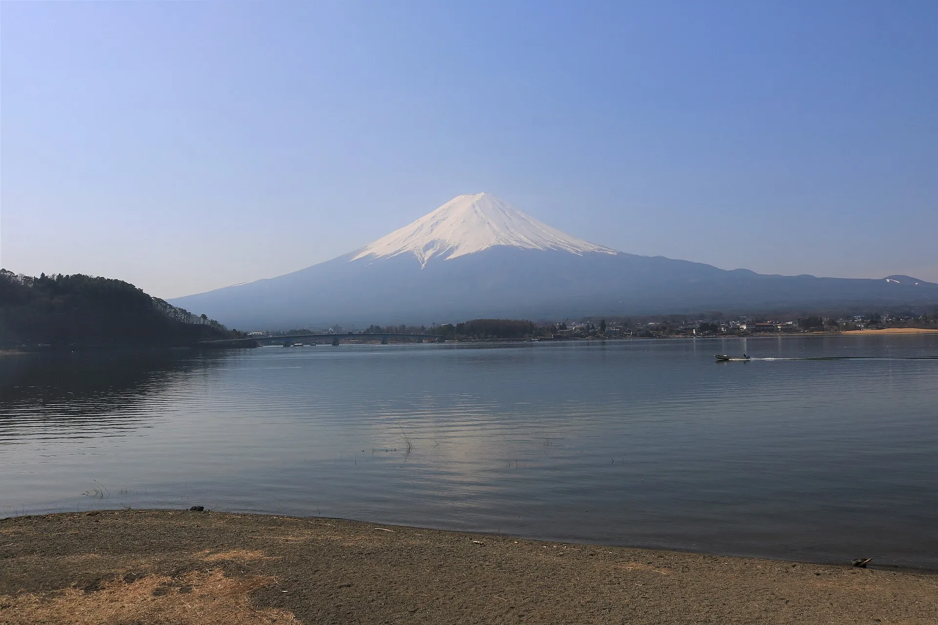 Snow-covered Mount Fuji above Lake Kawaguchi on a clear March morning, gravel shore in the foreground