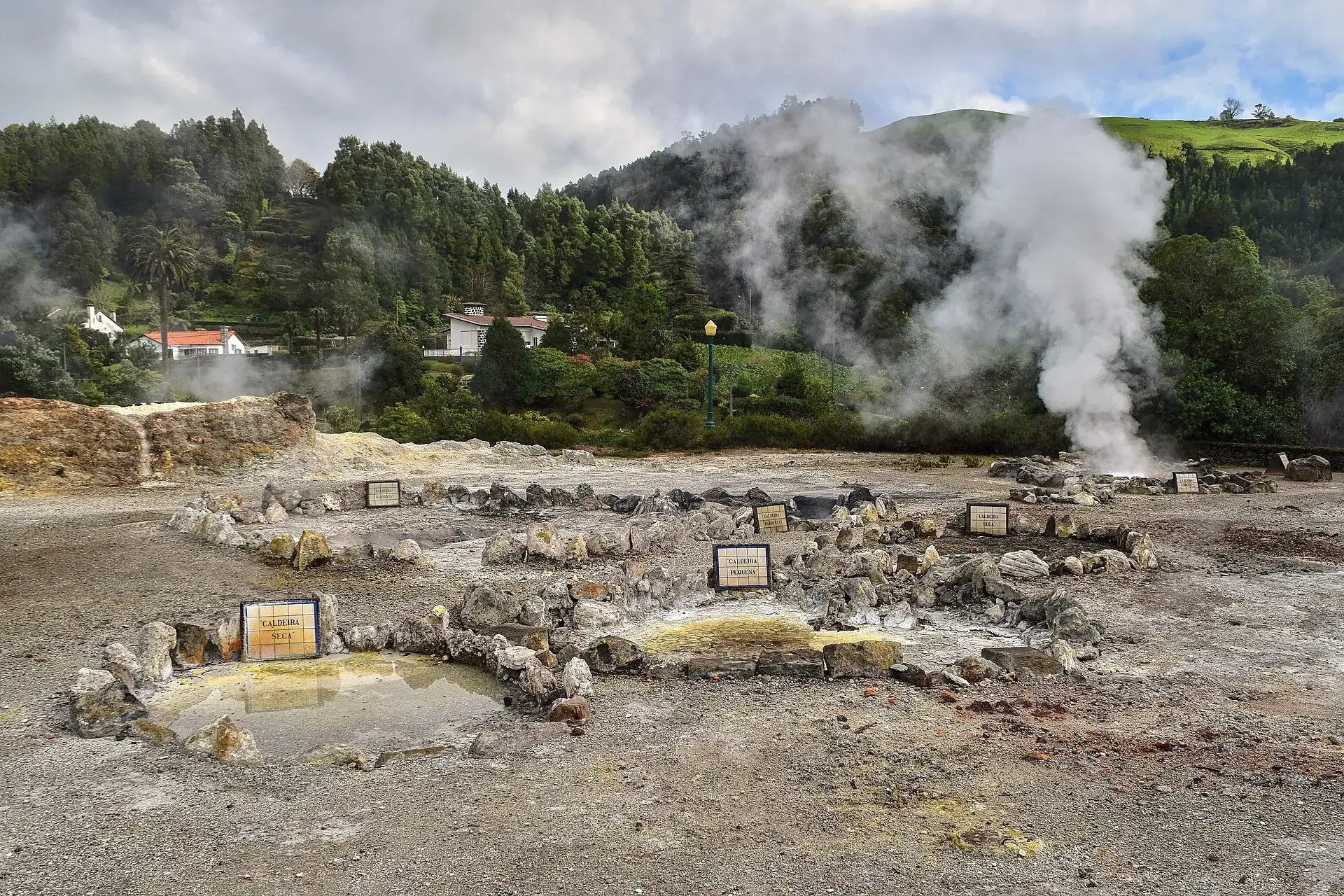 Die Caldeiras das Furnas mitten im Ort: dampfende Löcher im gelblichen Boden, umgeben von Steinmauern und grünen Hängen