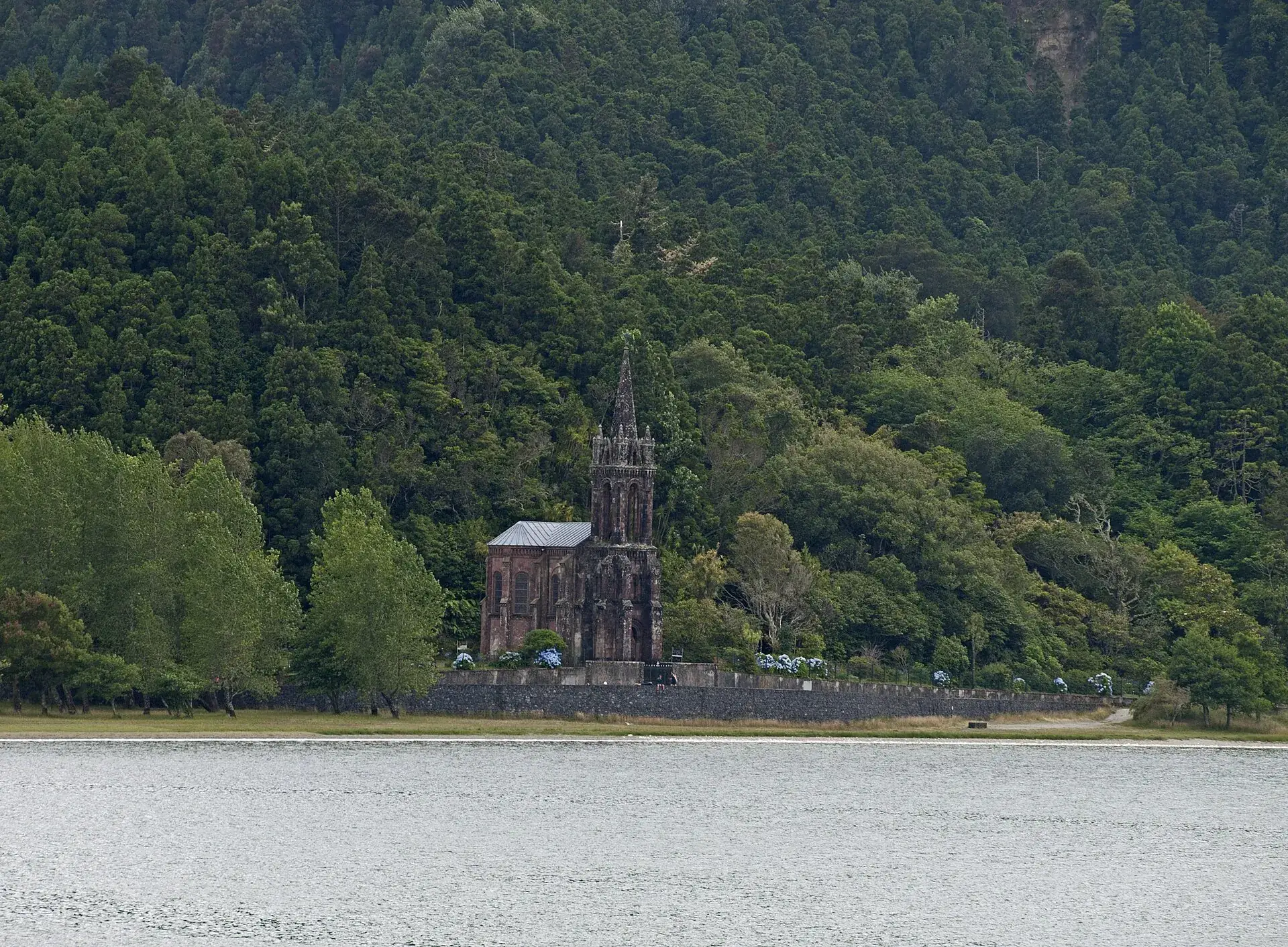 Die neugotische Kapelle Nossa Senhora das Vitórias am Westufer der Lagoa das Furnas, dahinter dichter Wald