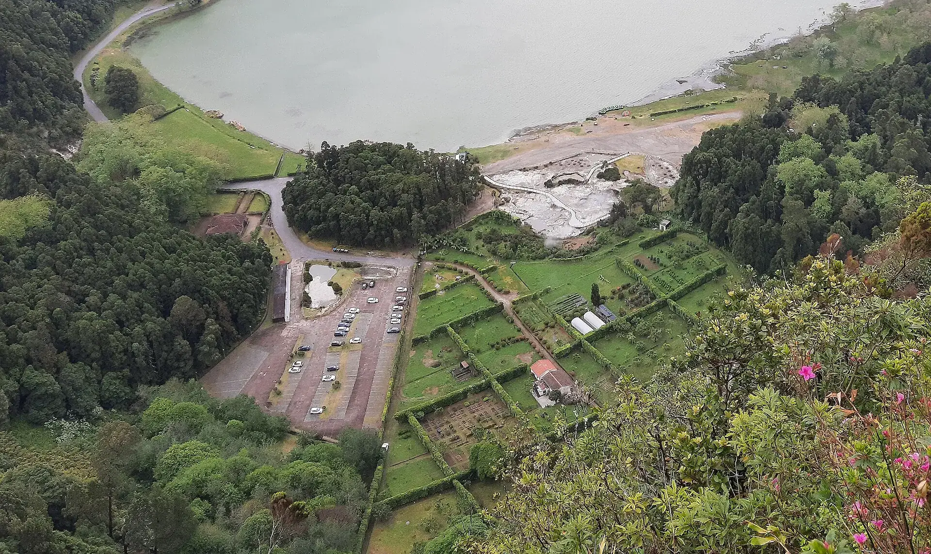 Die Kochgruben-Zone am Südufer der Lagoa das Furnas von oben: helles Fumarolenfeld, Parkplatz, Gärten und das braune Seeufer