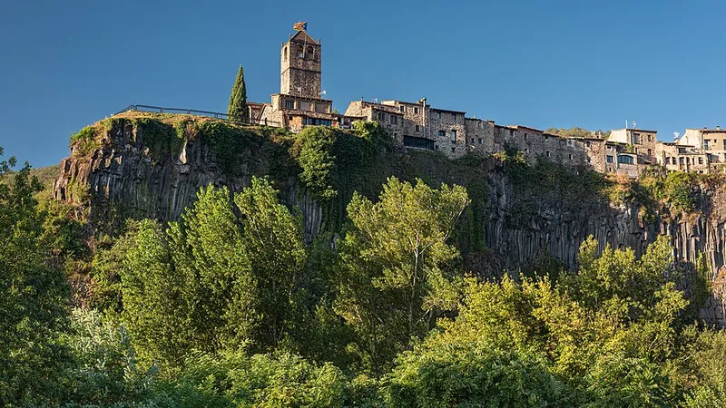 Castellfollit de la Roca: Häuser und Kirchturm auf der Kante einer dunklen Basaltklippe über dem Fluss
