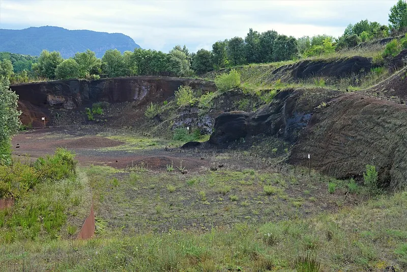 Die aufgeschnittene Nordostflanke des Croscat in der Garrotxa: rote und schwarze Lapilli-Schichten des alten Steinbruchs