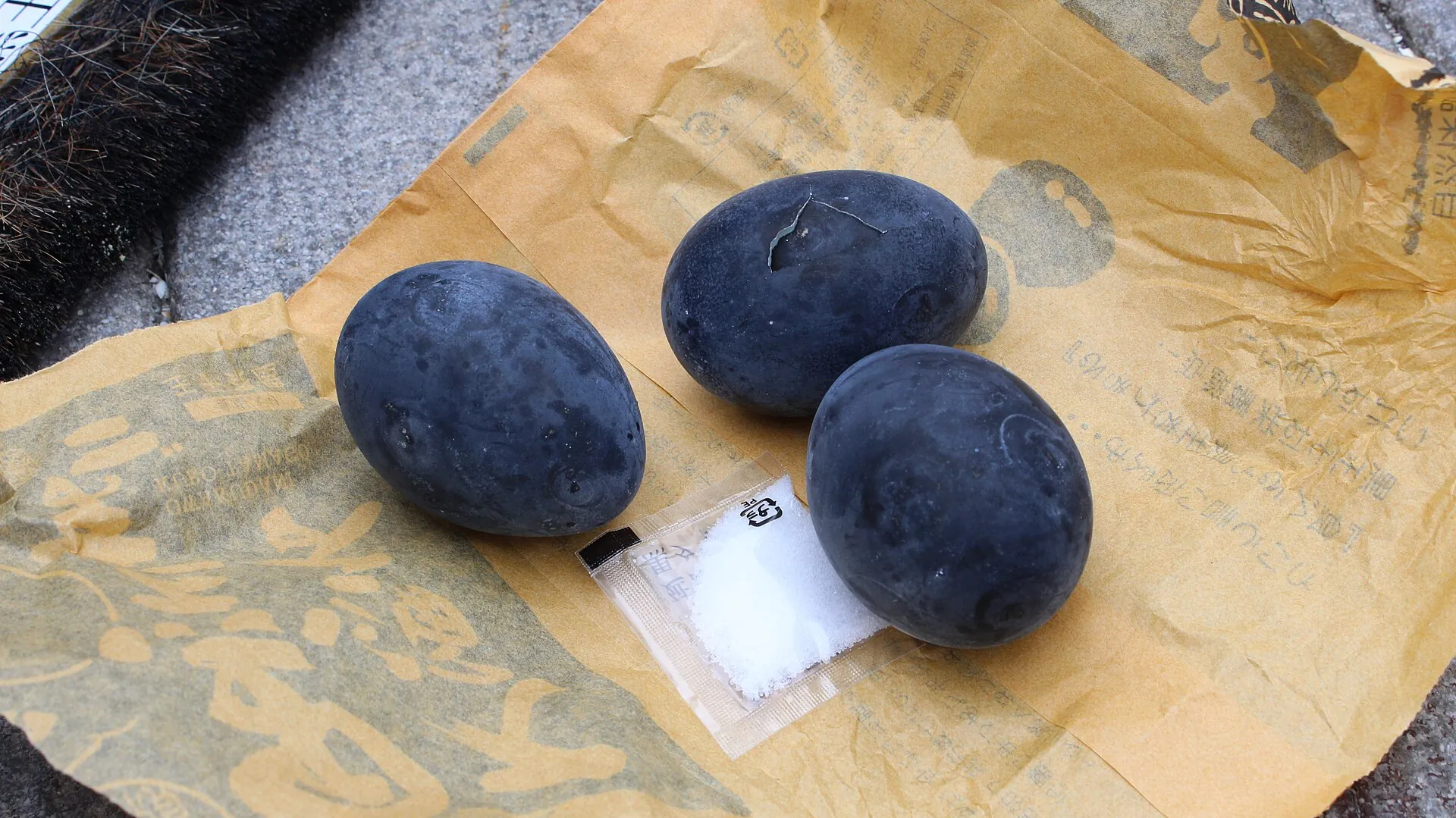 Three black eggs (kuro-tamago) from Ōwakudani with a small packet of salt on the vendor's paper bag