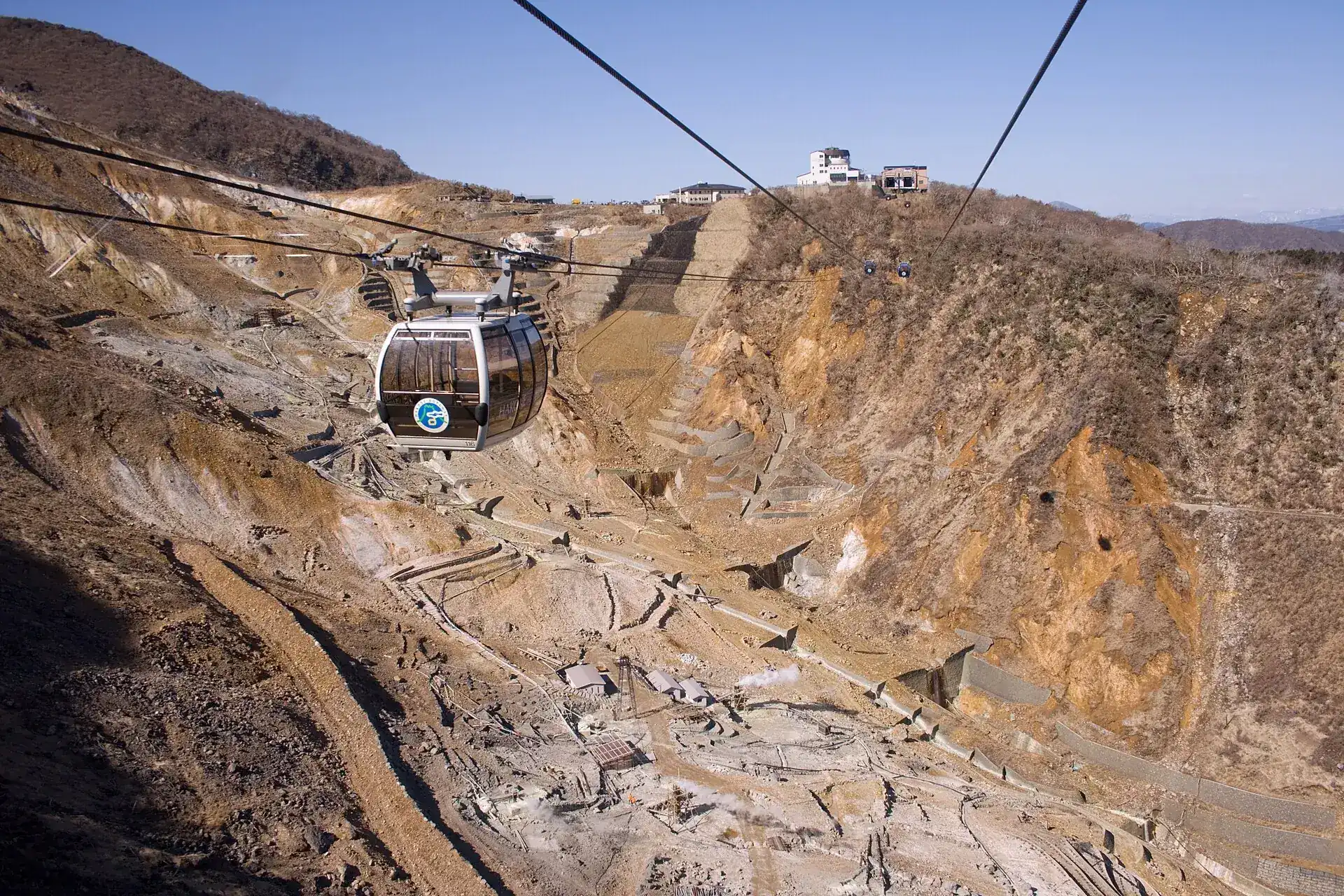 A Hakone Ropeway gondola above the bare, sulfur-yellow slope of Ōwakudani, with the station at the top