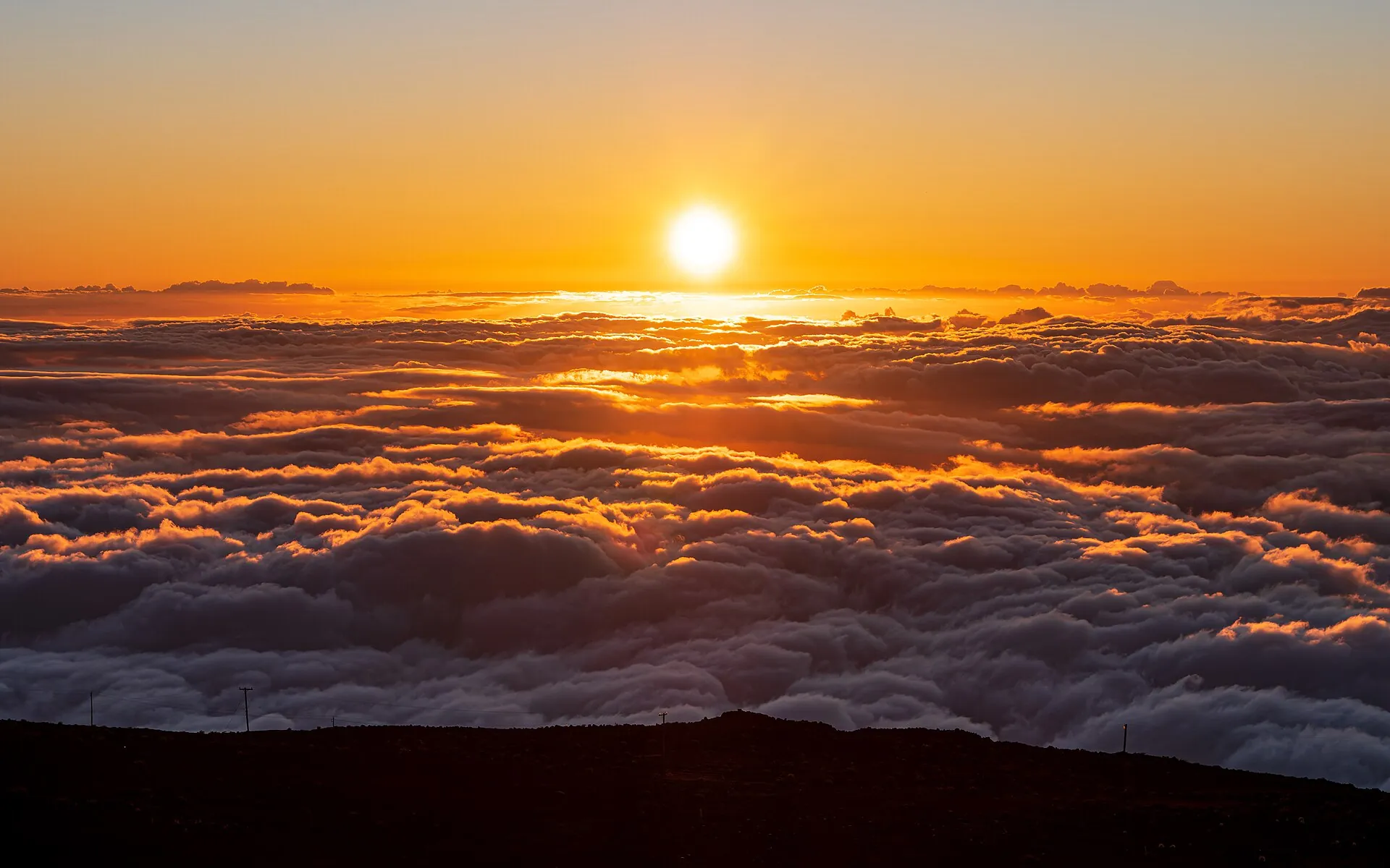 Sunset seen from Haleakalā: the sun sits just above a sea of clouds glowing orange