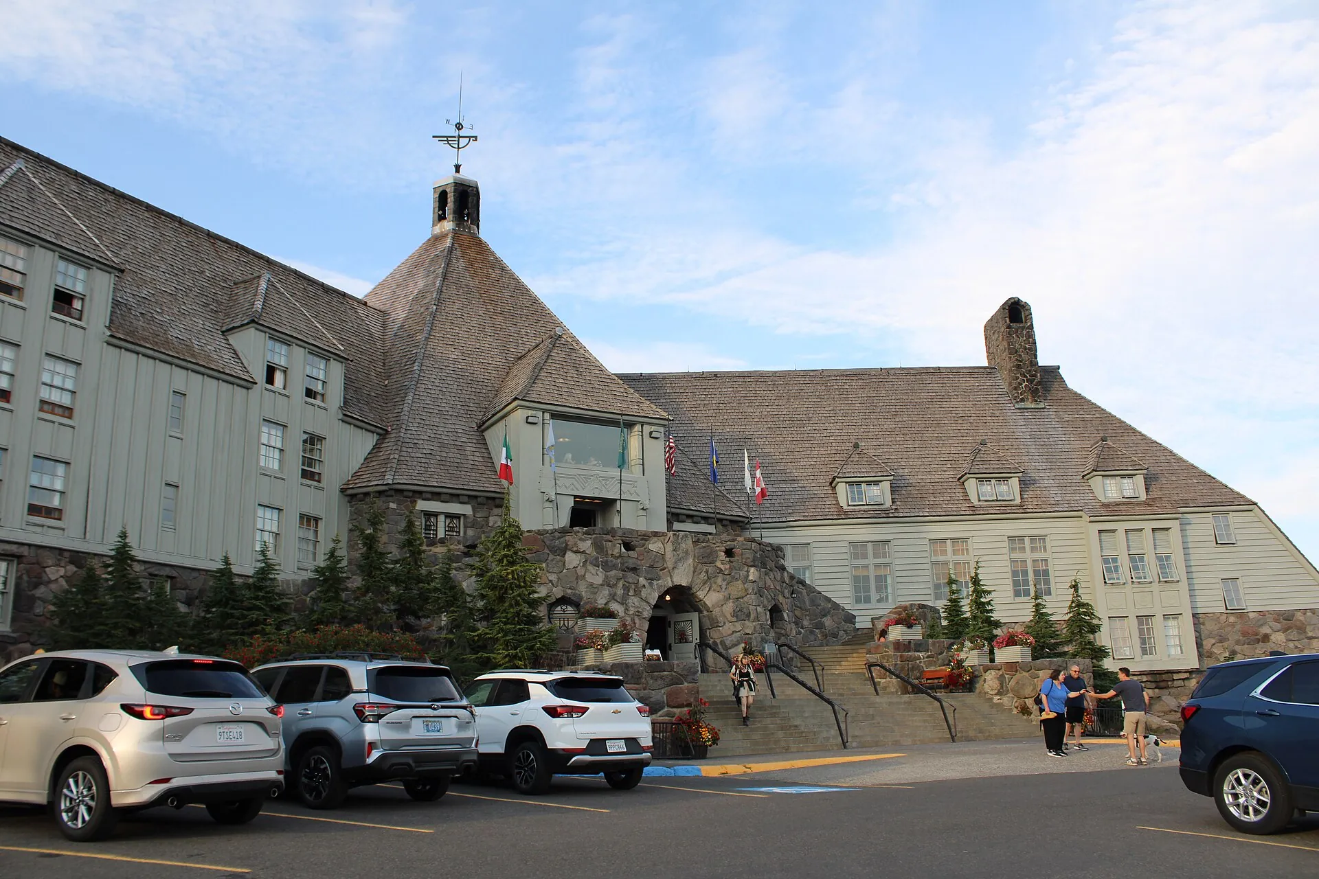 Die Timberline Lodge am Mount Hood von der Zufahrt aus: ein langgestreckter Holzbau mit steilem Schindeldach und steinernem Kaminturm, davor geparkte Autos und Besucher auf der Freitreppe