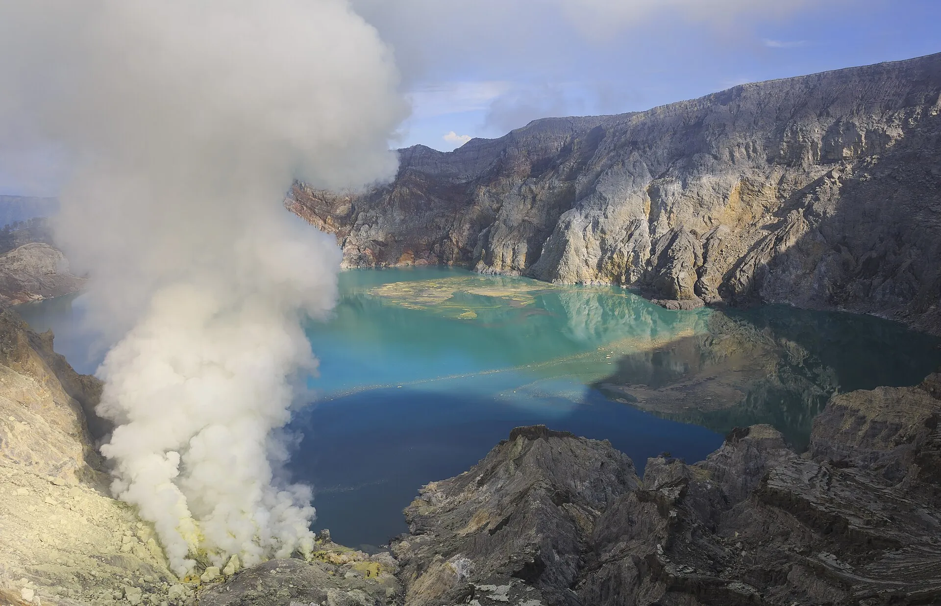 View from the crater rim of Kawah Ijen: a dense yellow-white cloud of sulfur steam rises next to the turquoise acid lake