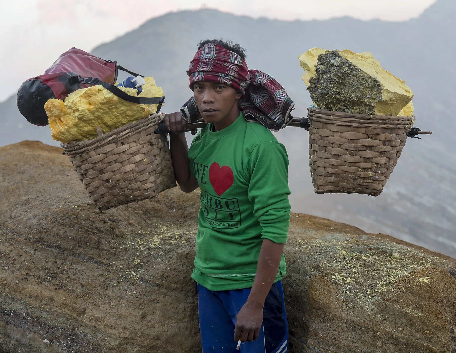 A sulfur carrier at Kawah Ijen carries two baskets filled with yellow sulfur chunks on a pole over his shoulder