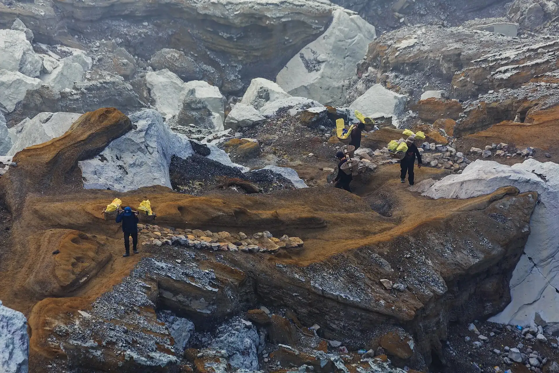 Sulfur carriers with yellow-filled baskets on the rocky path in the crater of Kawah Ijen