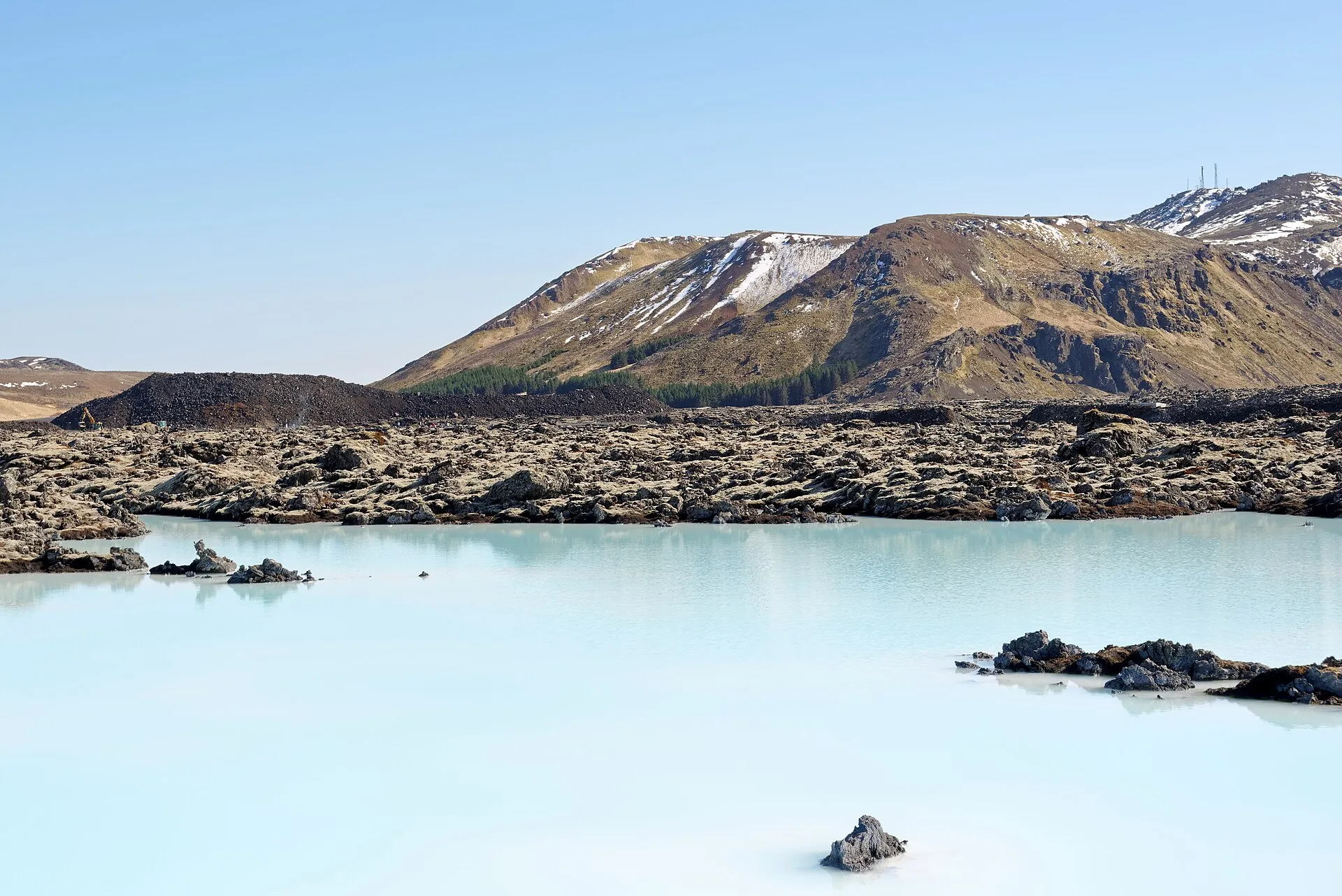 The milky-blue Blue Lagoon in front of black lava, the mountain Þorbjörn with patches of snow behind