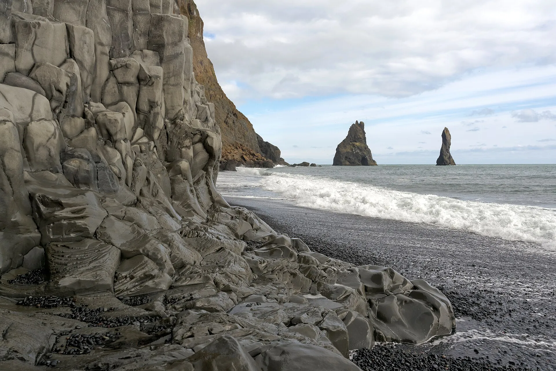 The basalt columns on Reynisfjara beach, black sand in front, the Reynisdrangar sea stacks in the background