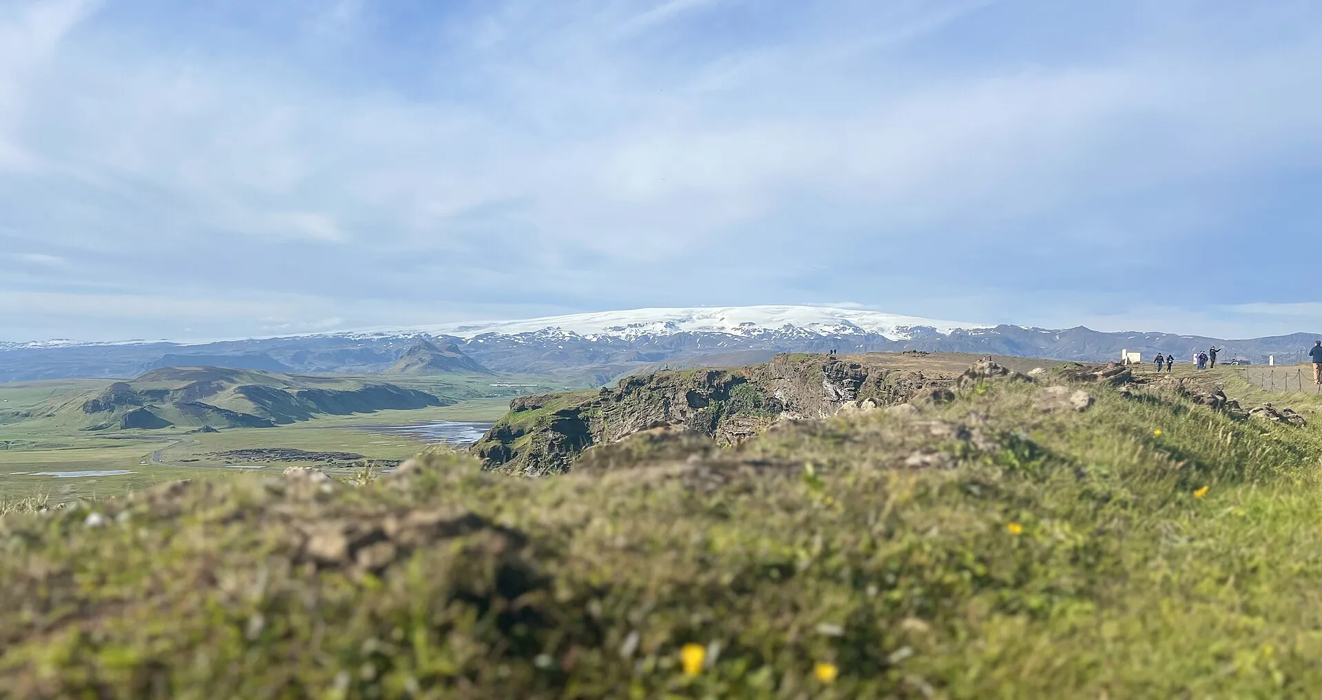 View north from Dyrhólaey: green hills, behind them the white ice cap of Mýrdalsjökull covering the Katla volcano