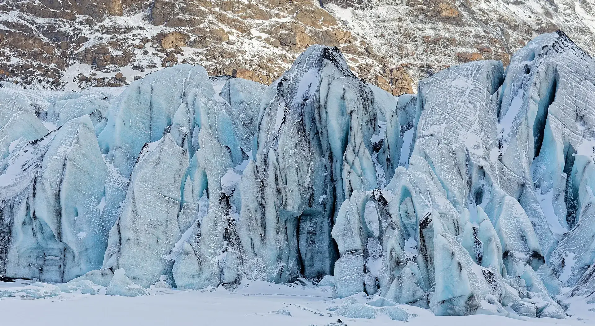 The fractured ice wall of Sólheimajökull up close, blue and white with dark bands of ash