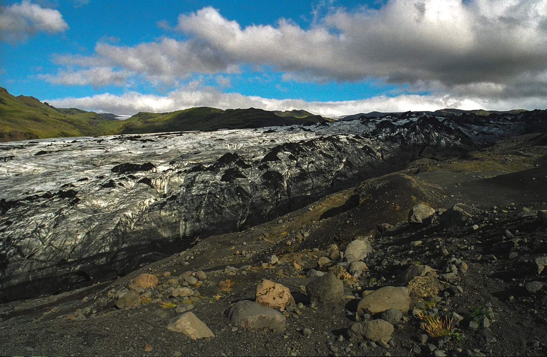 The tongue of the Sólheimajökull glacier, black with volcanic ash, under a cloudy sky
