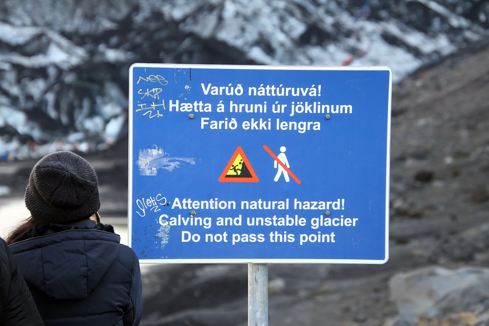 Blue warning sign at Sólheimajökull: “Attention natural hazard! Calving and unstable glacier – do not pass this point”, the glacier behind it