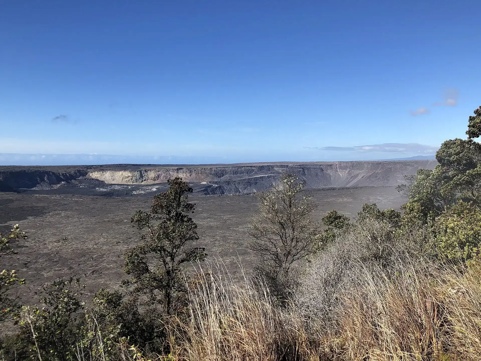 Kīlauea's summit caldera by day, seen from Wahinekapu across the gray caldera floor toward the collapsed Halemaʻumaʻu crater