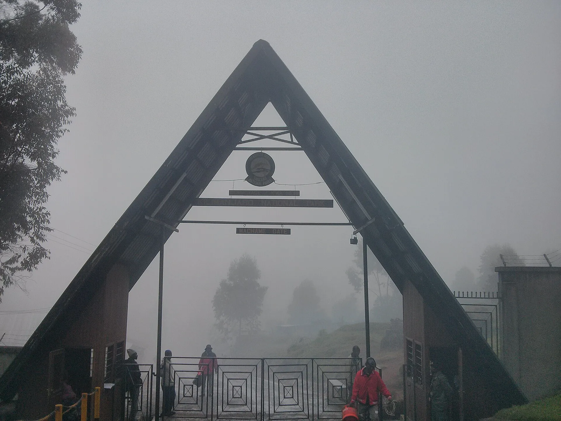 The wooden A-frame gate of the Machame route on Kilimanjaro in morning mist, hikers at the turnstile